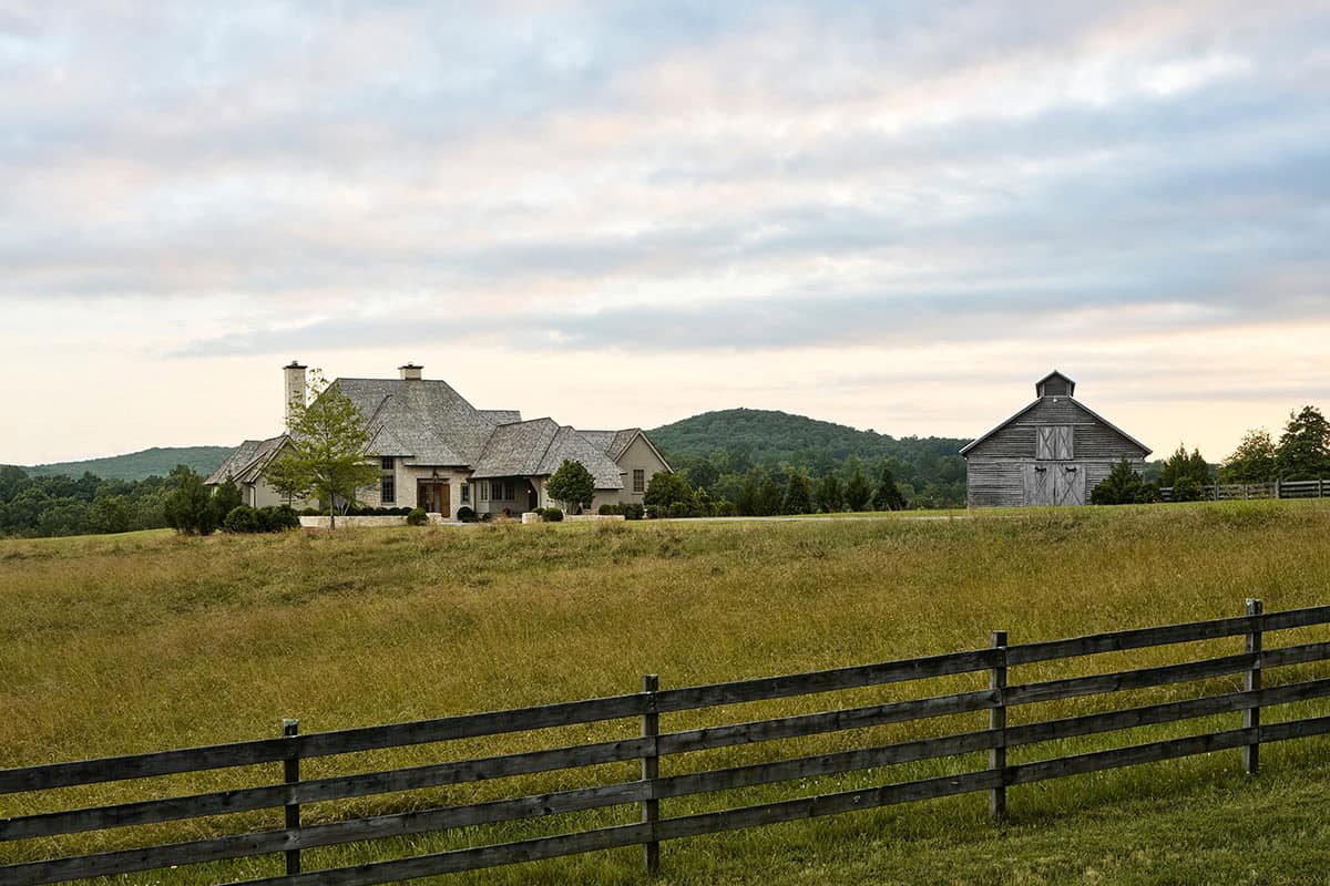 Wide view of farmhouse and rustic barn across pastoral fenced field