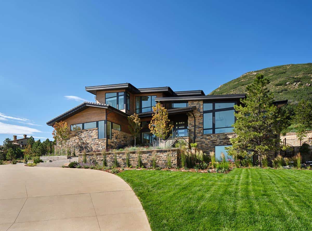 Mountain modern home exterior with stone and wood siding, curved driveway, and mountain backdrop
