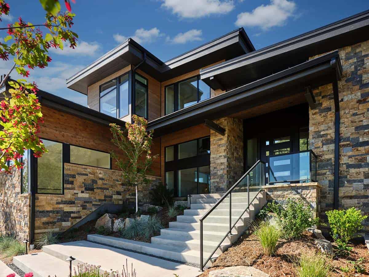 Close-up of home entry with cantilevered roof, stone columns, and glass railing staircase