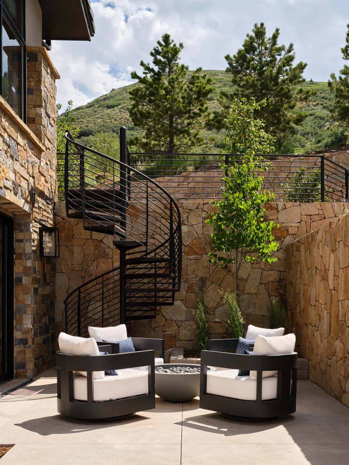 Outdoor patio with black spiral staircase, stone walls, and round fire pit seating