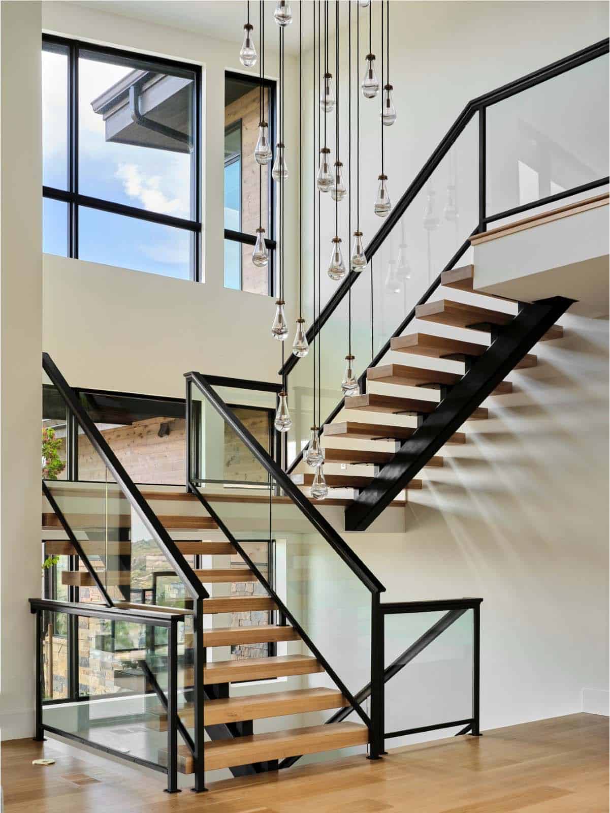 Two-story staircase with black metal railings, wood treads, and hanging glass pendant lights