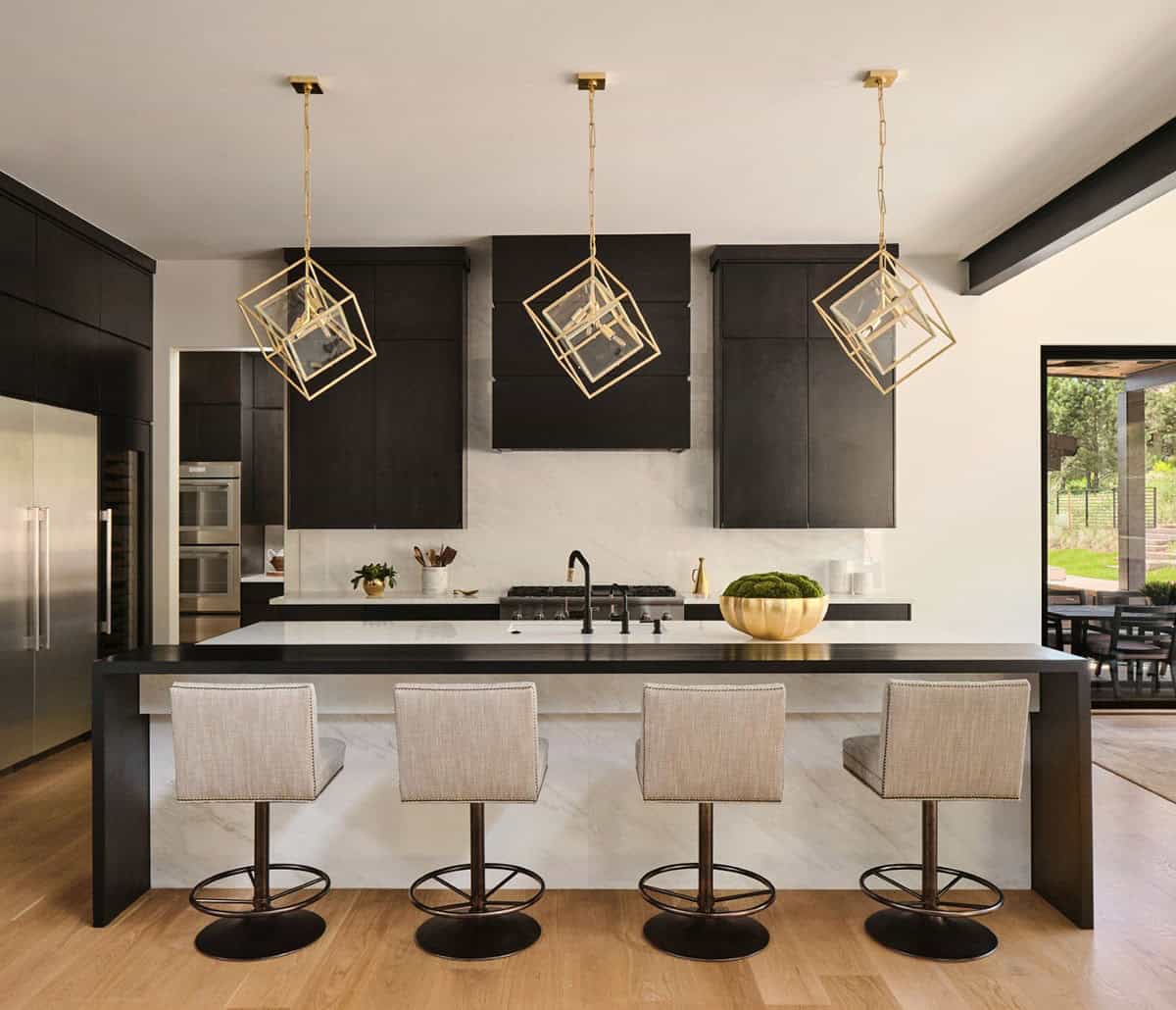 Kitchen island with marble countertop, dark cabinetry, and geometric brass pendant lights
