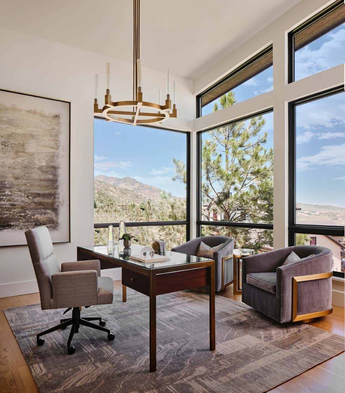 Home office with glass-top desk, velvet chairs, and floor-to-ceiling mountain-view windows