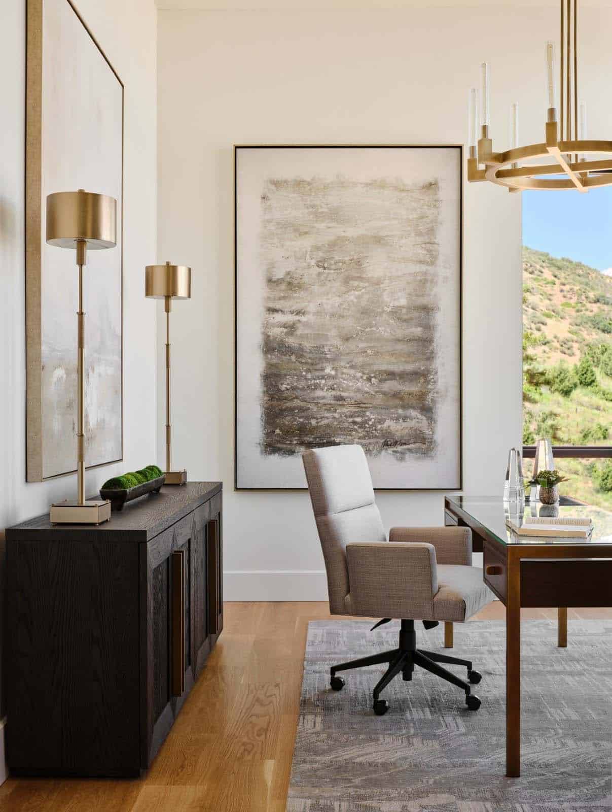 Home office vignette with dark sideboard, brass table lamps, and abstract landscape painting