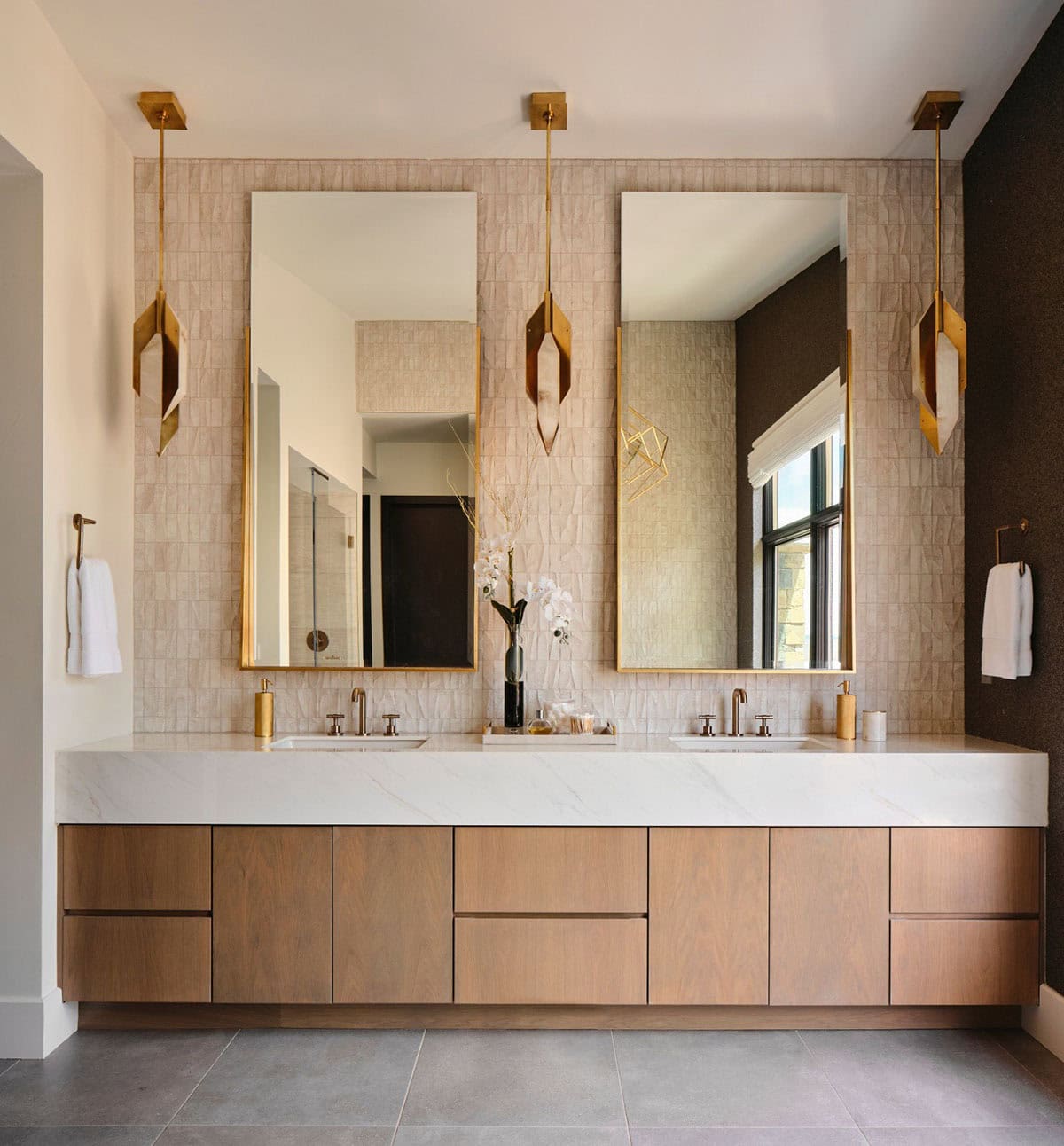 Double bathroom vanity with textured tile wall, gold mirrors, and hanging brass sconces