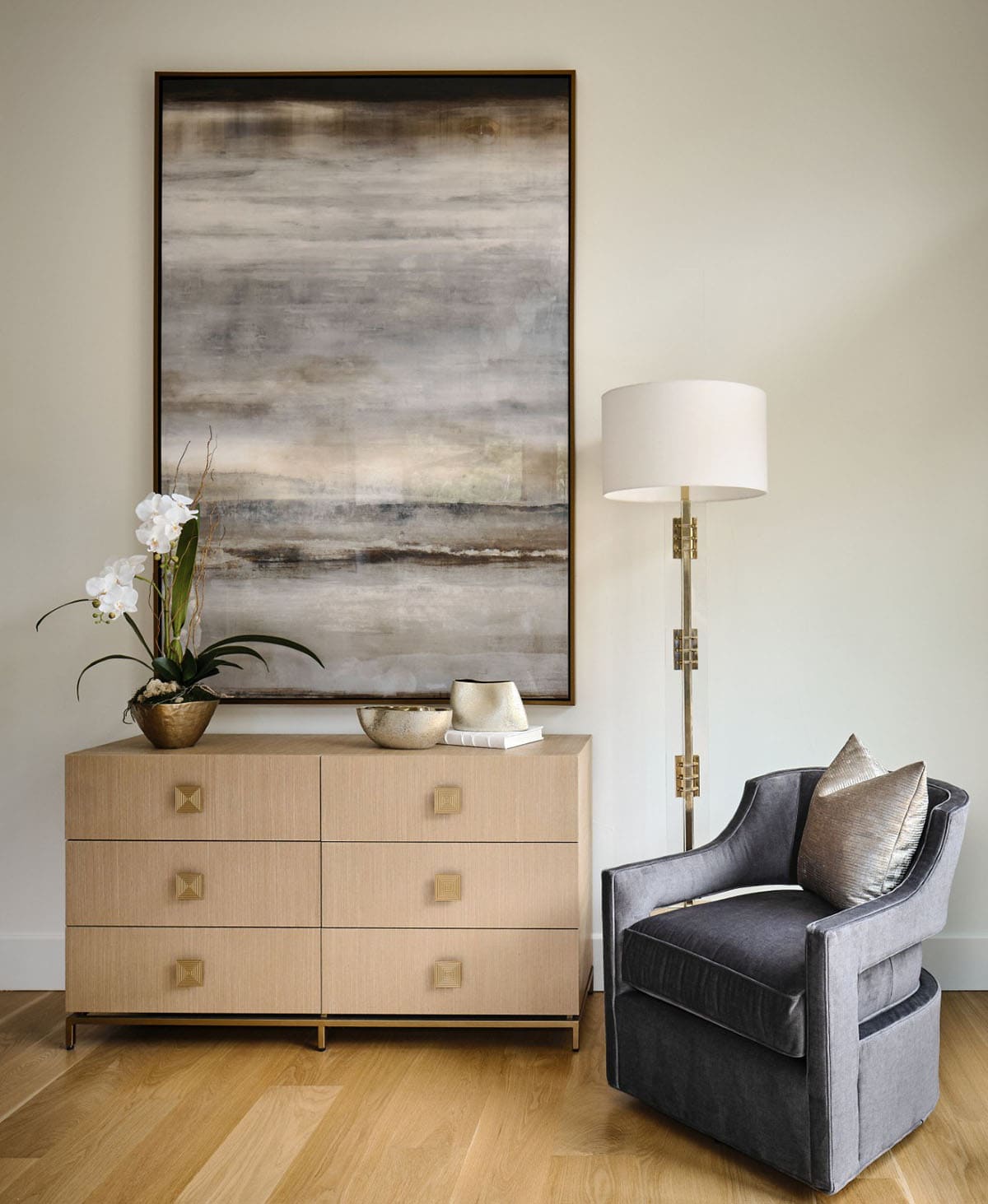 Living area vignette with abstract art, brass floor lamp, and gray swivel chair