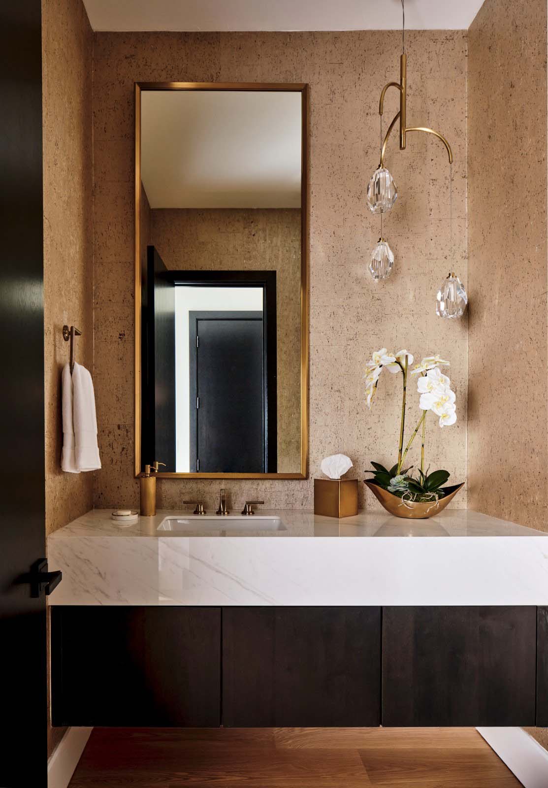 Powder room with textured tan wallpaper, brass-framed mirror, and crystal teardrop pendants