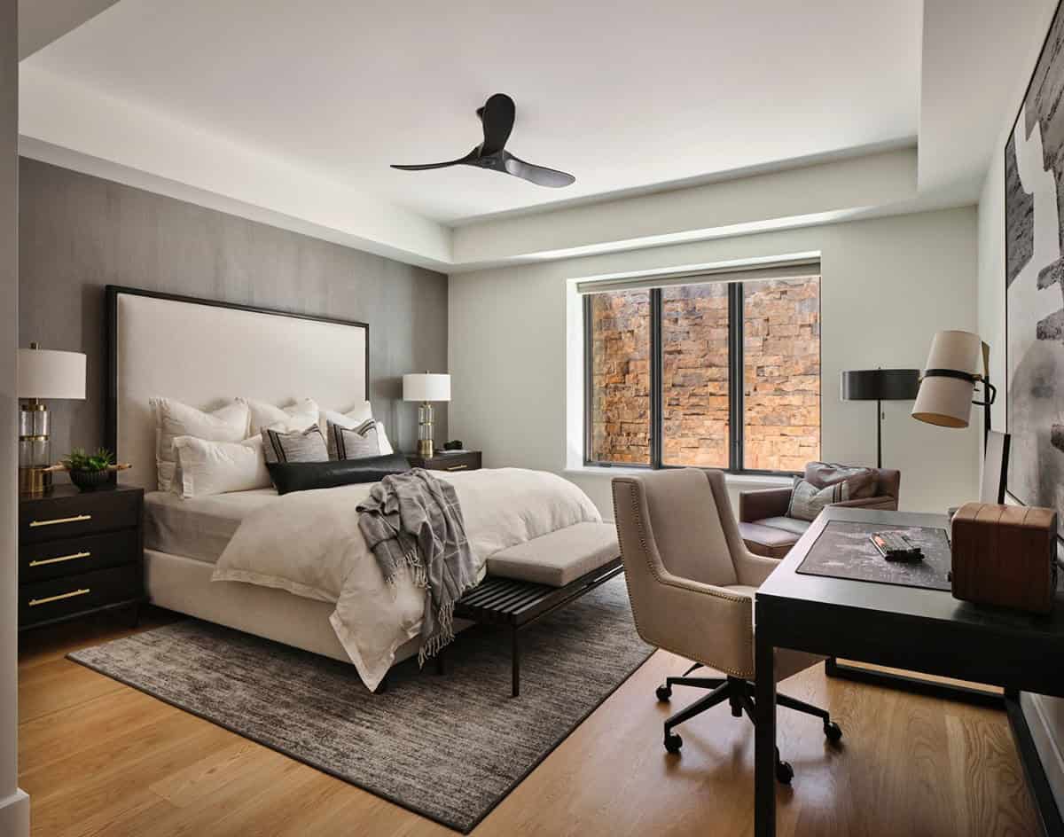 Bedroom with dark accent wall, ceiling fan, and stacked-stone exterior view through window