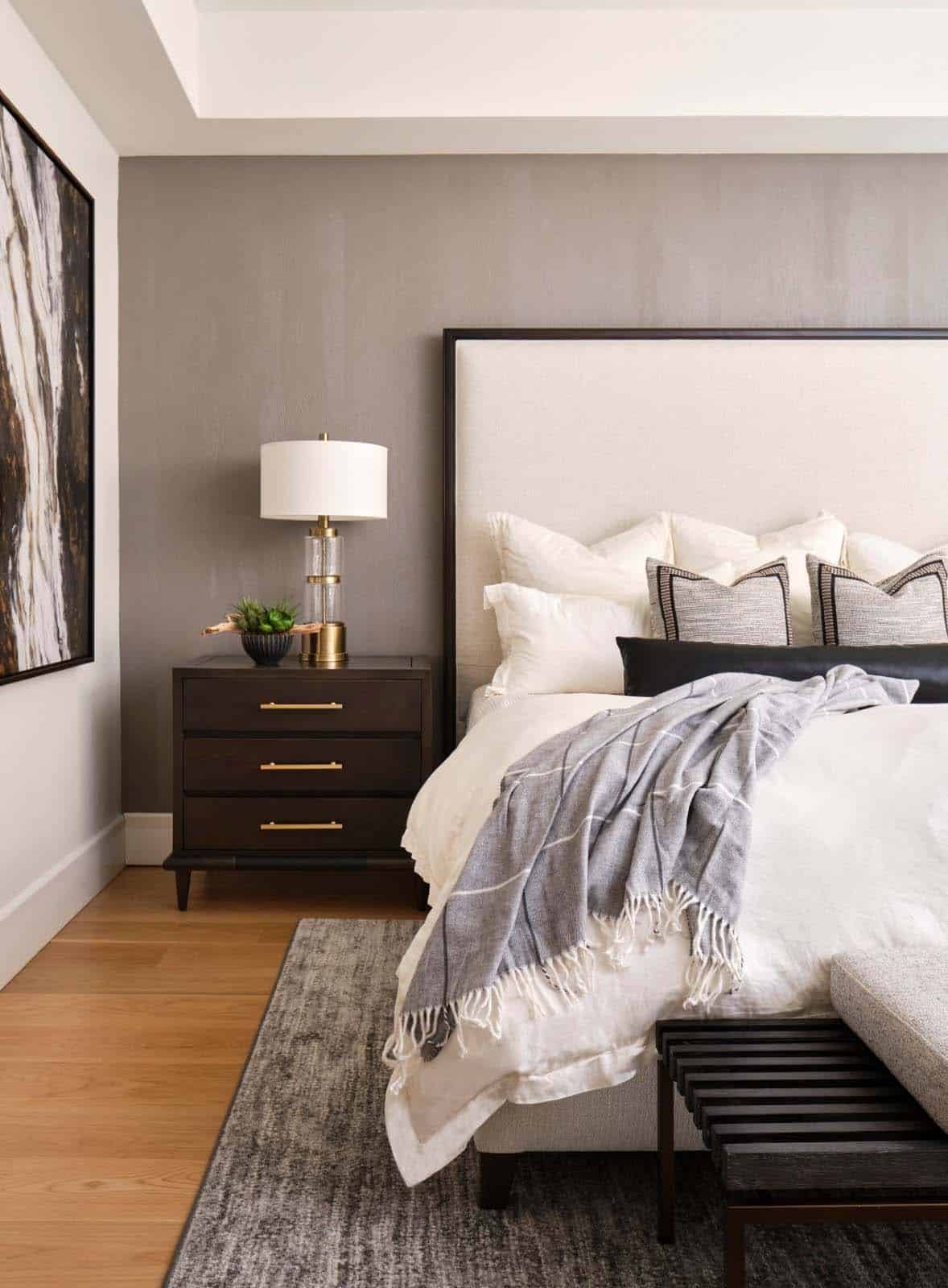 Bedside detail with dark wood nightstand, glass table lamp, and layered white bedding