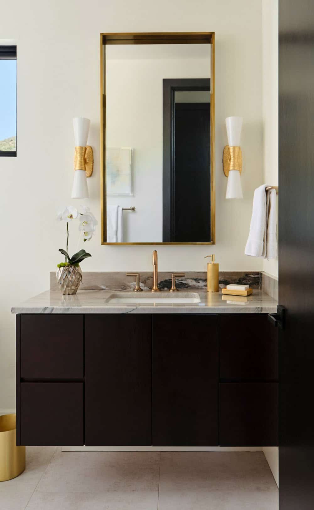 Bathroom vanity with dark cabinetry, brass-framed mirror, and hourglass wall sconces
