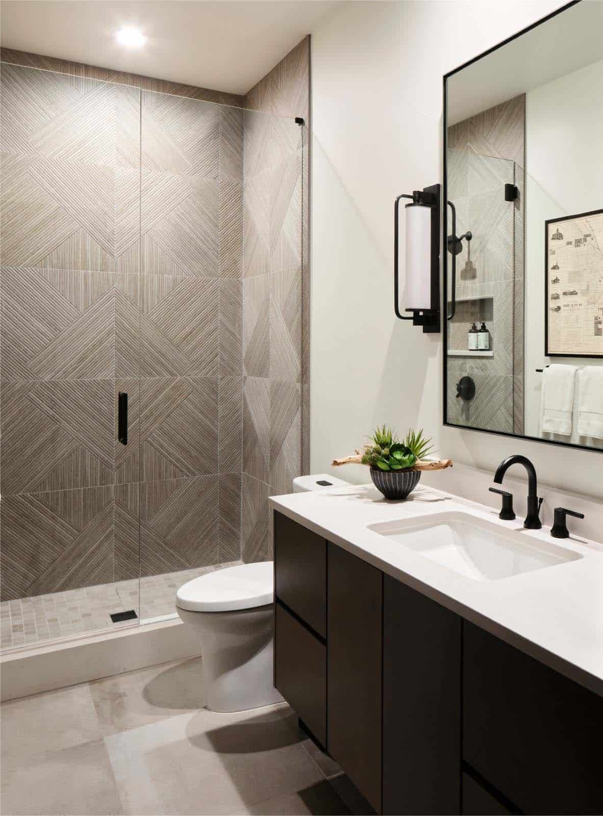 Bathroom with dark vanity, geometric tiled shower, and black-framed mirror