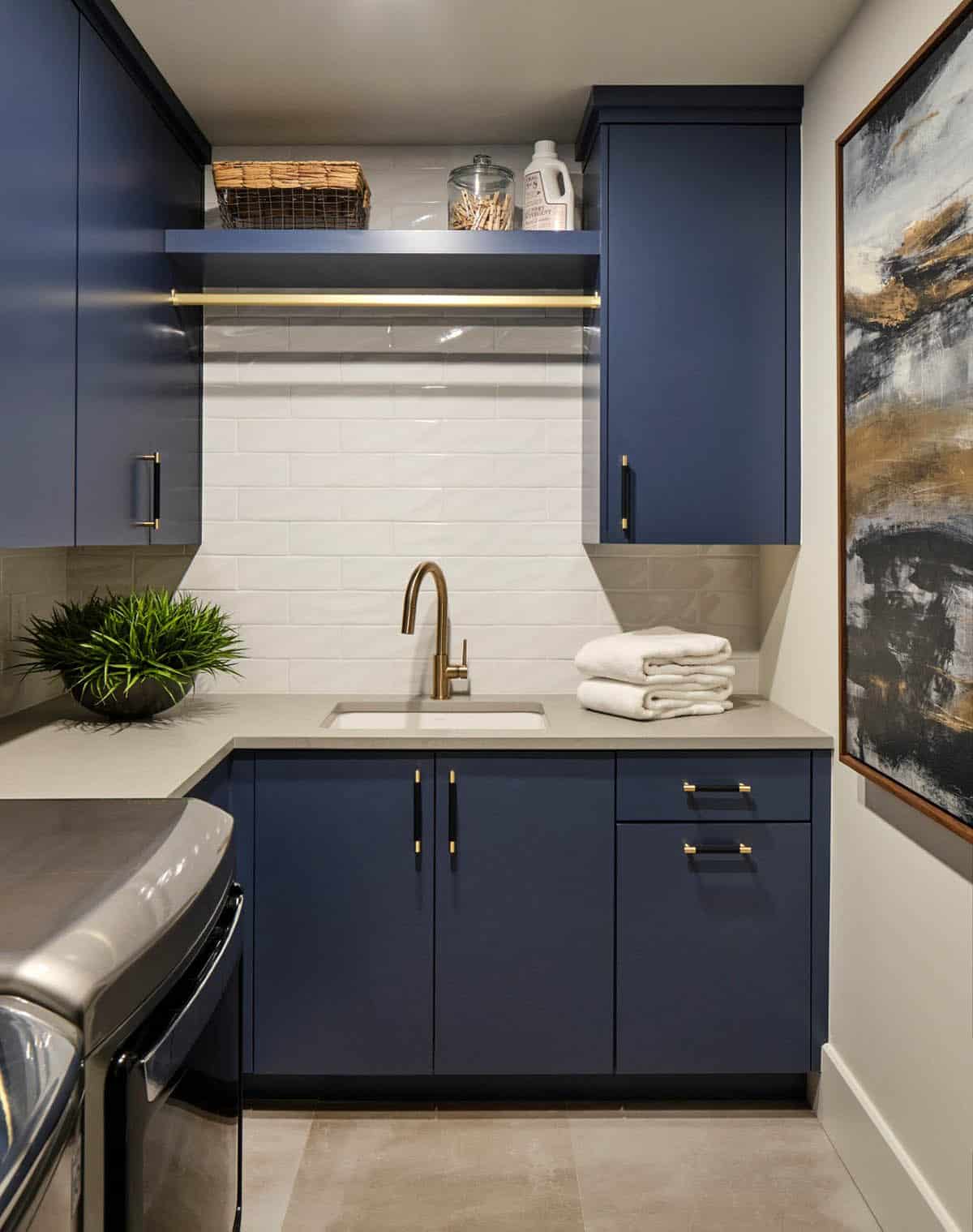 Laundry room with navy cabinetry, brass faucet, and white subway tile backsplash
