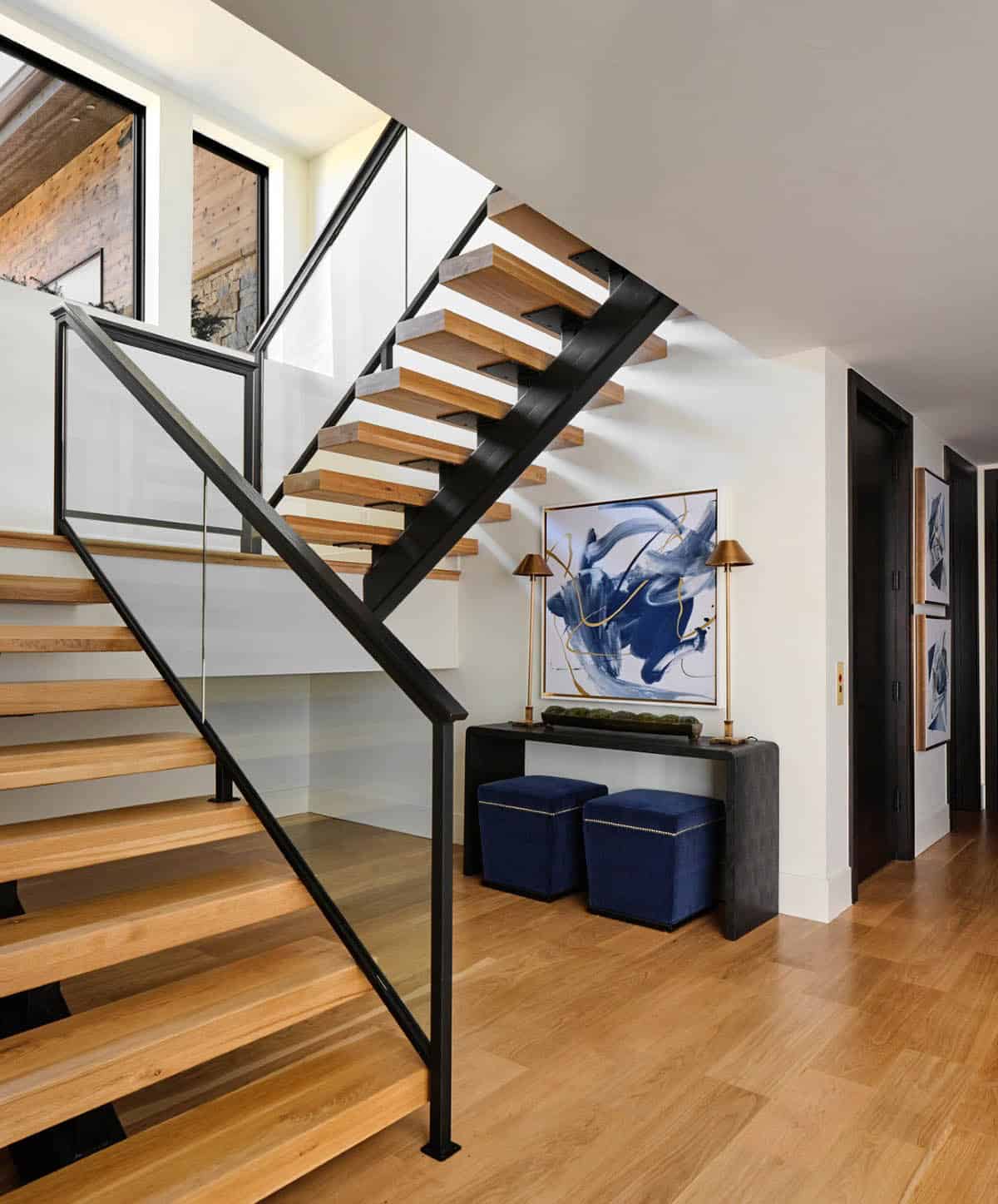 Basement staircase landing with console table, blue abstract art, and navy velvet ottomans