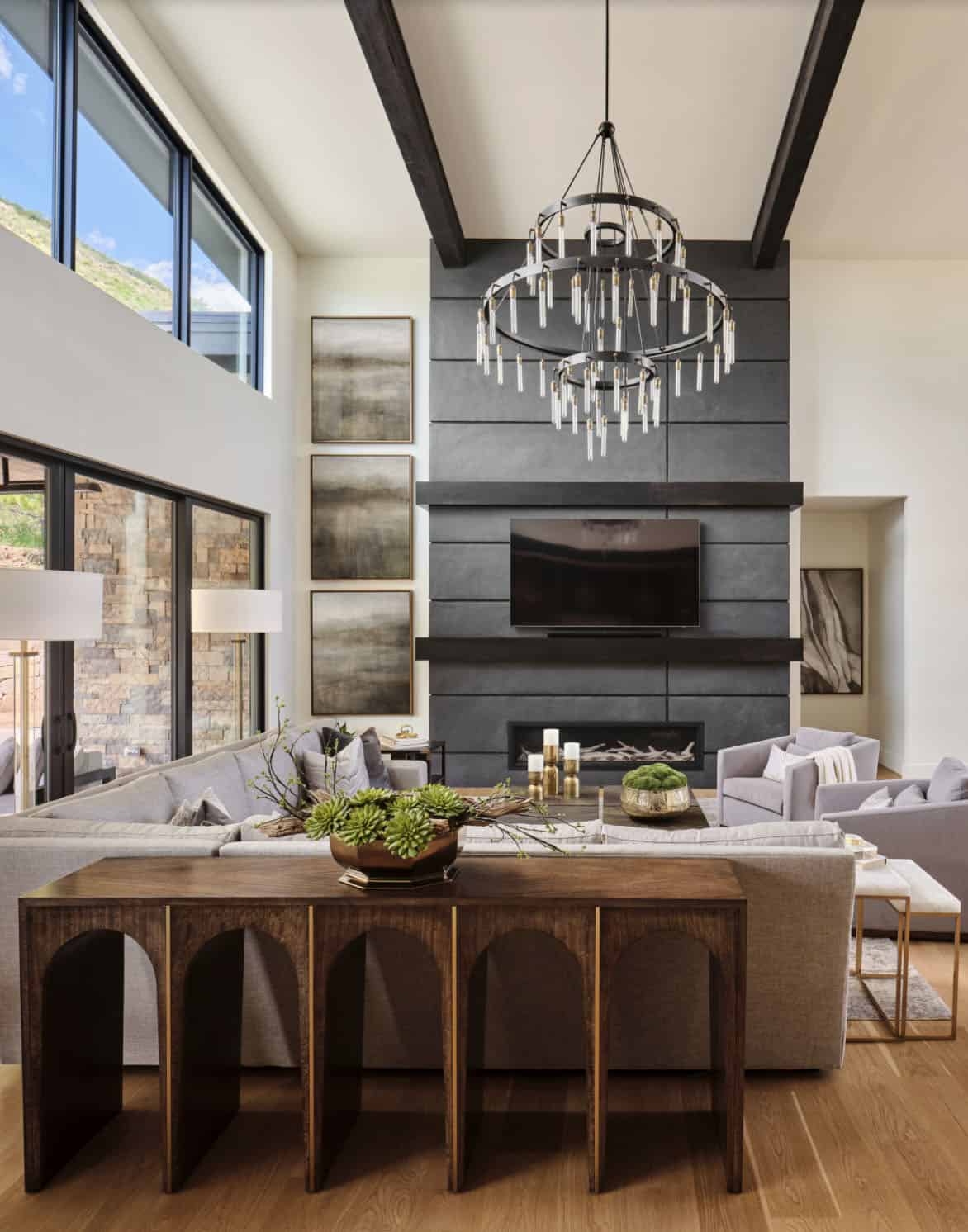 Great room with dark shiplap fireplace wall, layered chandelier, and console table with succulents