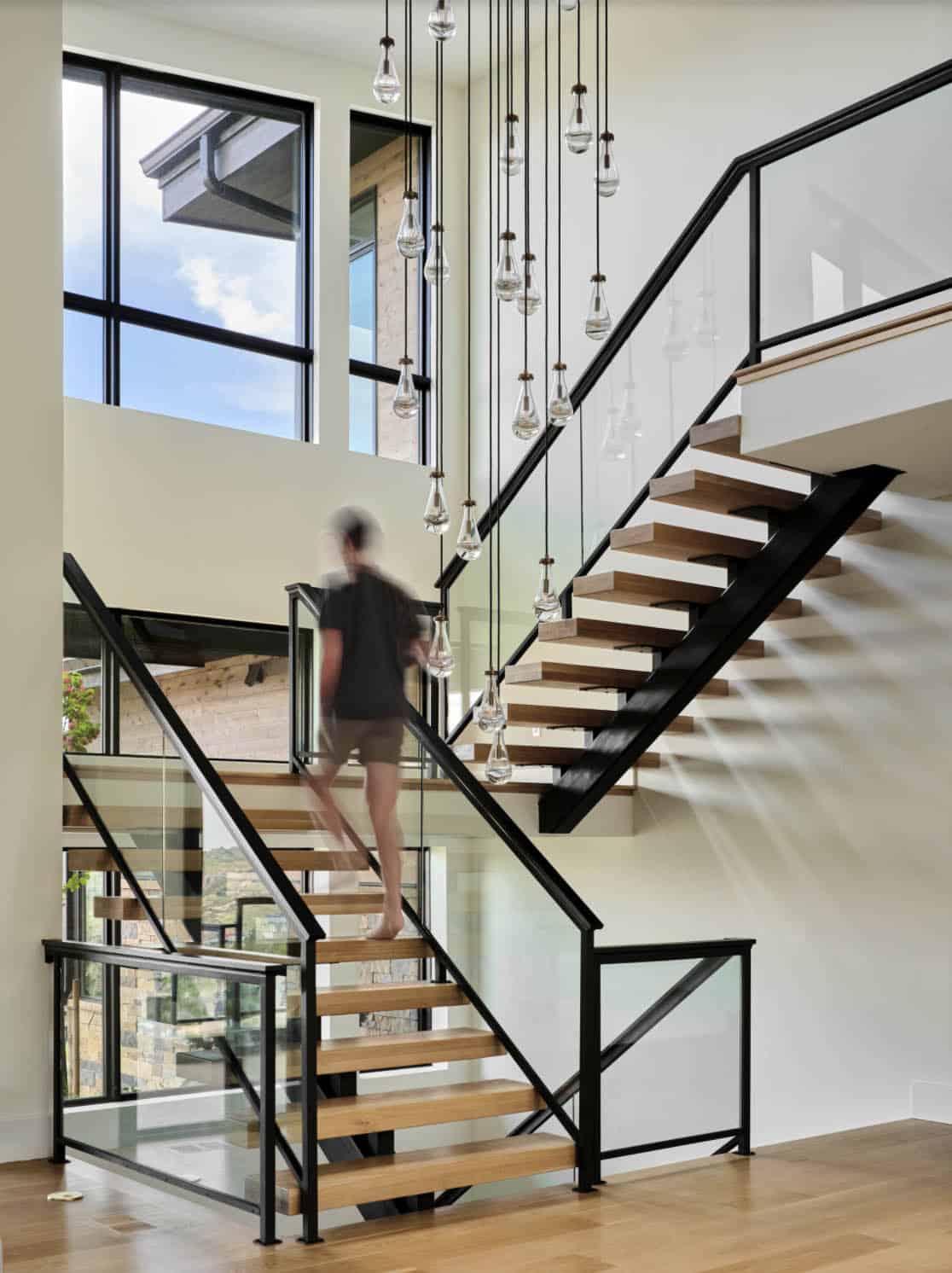 Multi-level staircase with glass railings, wood treads, and cascading glass pendant lights