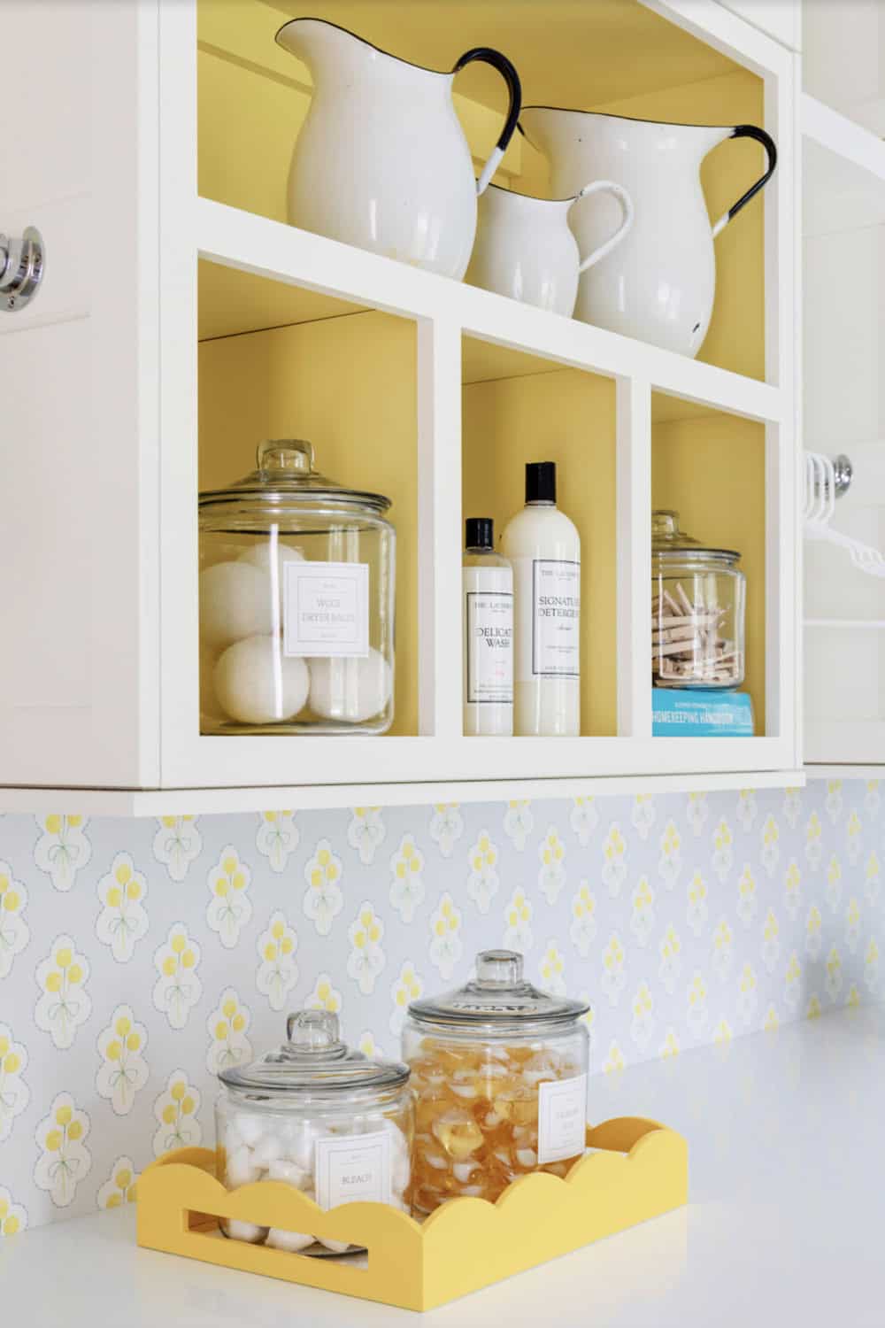 Open laundry cabinet storing pitchers, detergent, dryer balls, and clothespins