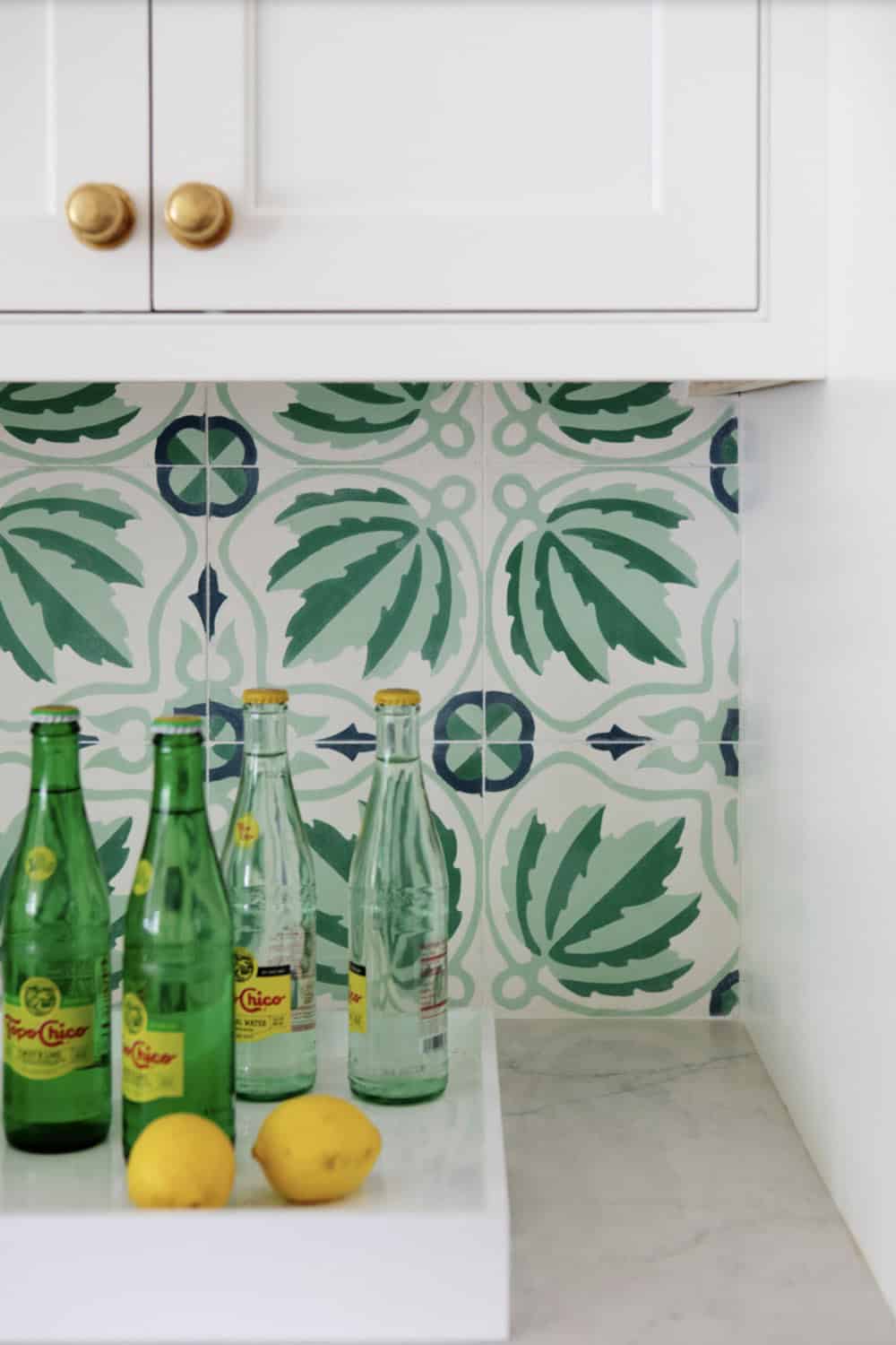 Sparkling water bottles and lemons against green leaf tile backsplash