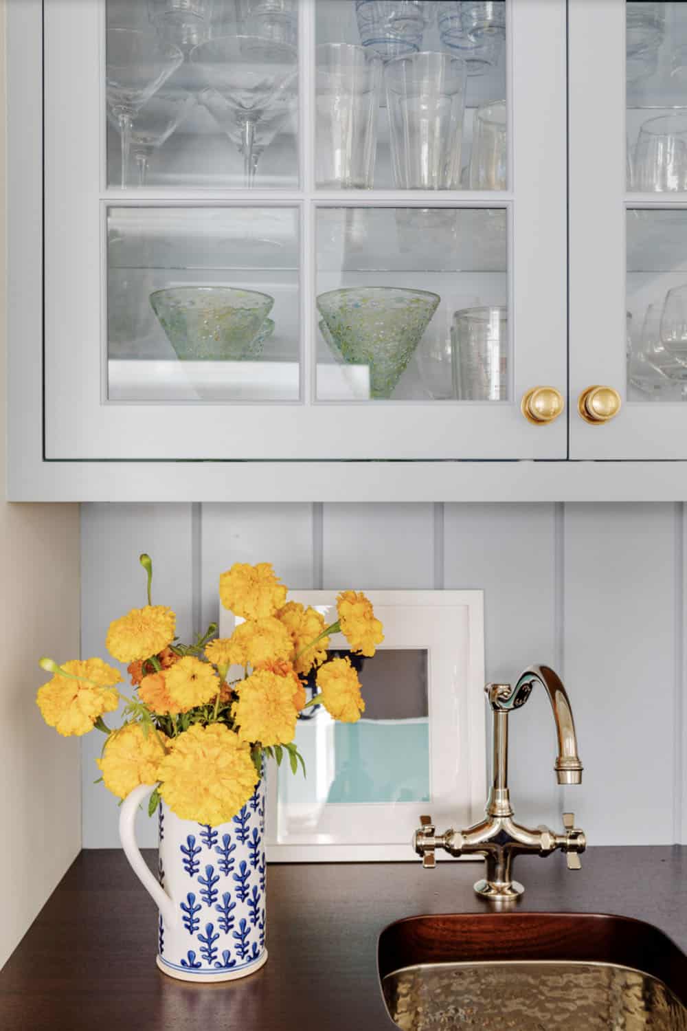 Marigolds in blue pitcher beside glass front pantry cabinet doors