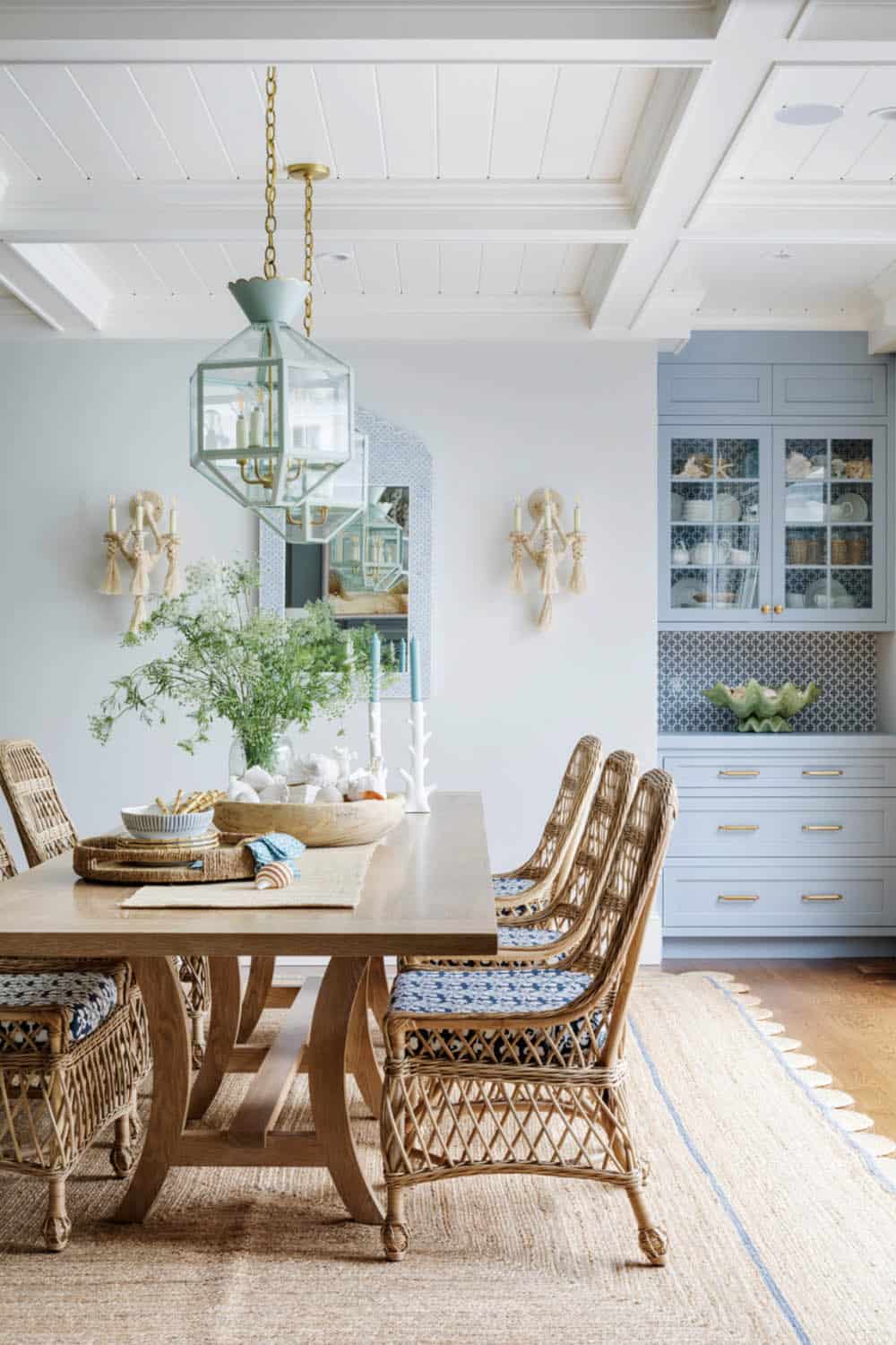 Dining room with rattan chairs, blue hutch, and lantern pendants