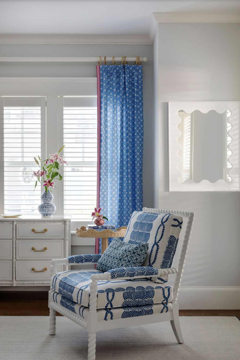 Blue and white armchair beside dresser and scalloped mirror
