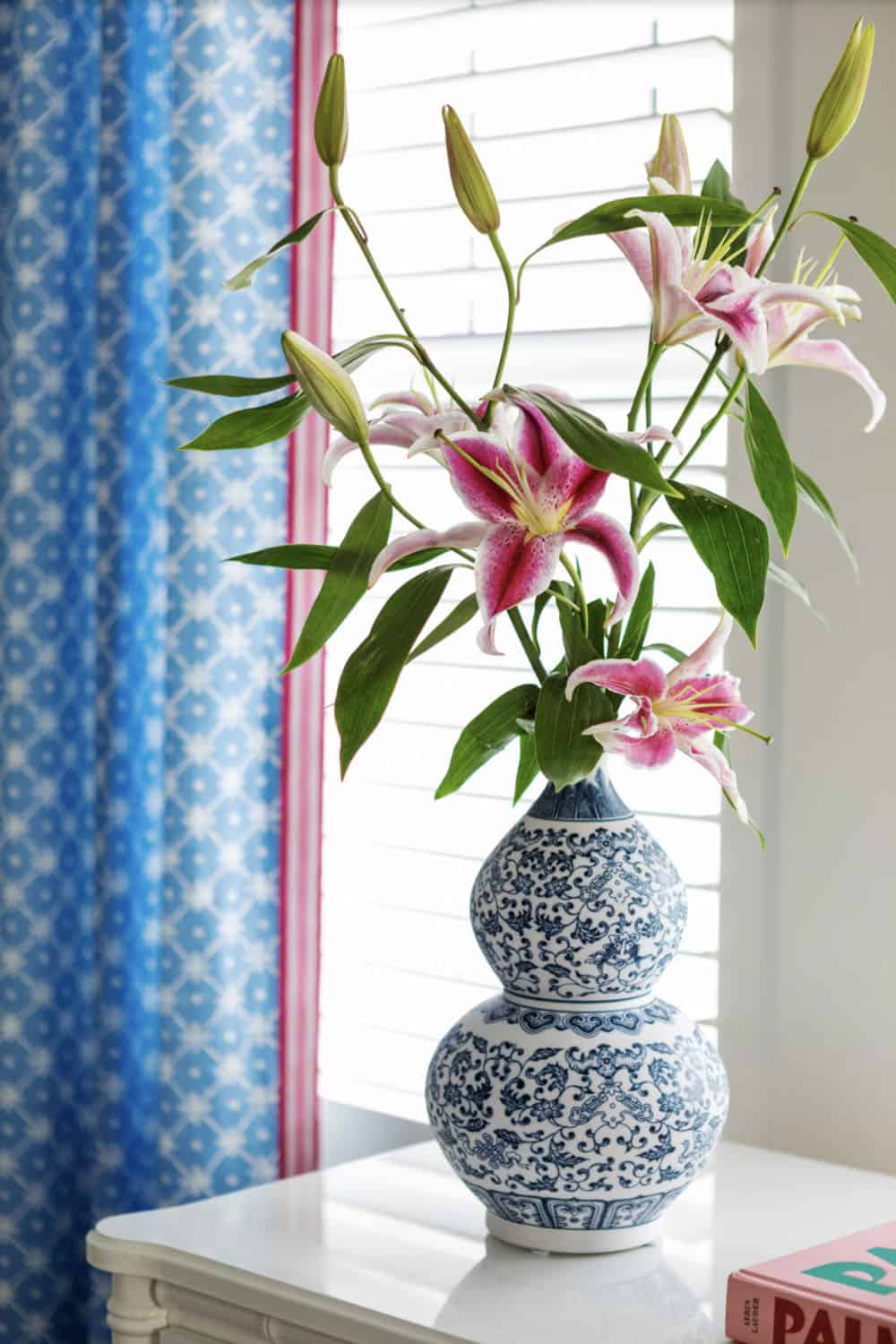 Stargazer lilies in blue and white vase near patterned curtain