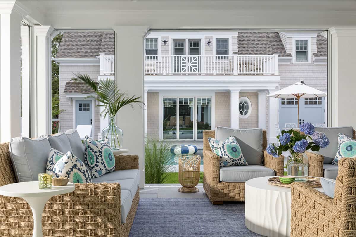 Covered porch with woven armchairs facing pool and rear facade