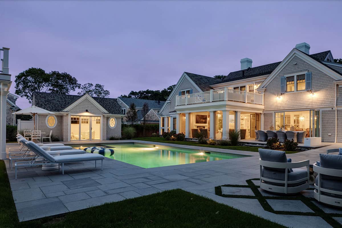 Poolside patio with lounge chairs and pool house at twilight