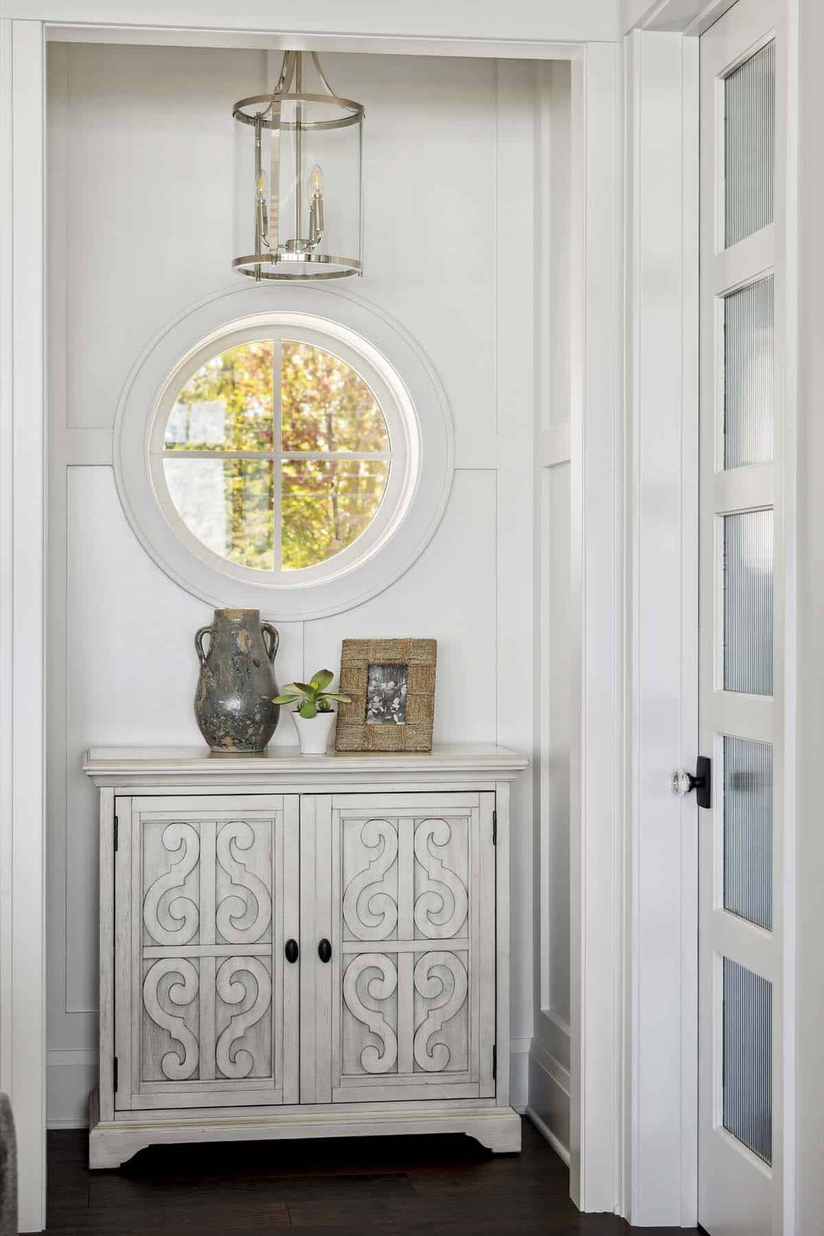 Foyer niche with round window, pendant light, and carved accent cabinet