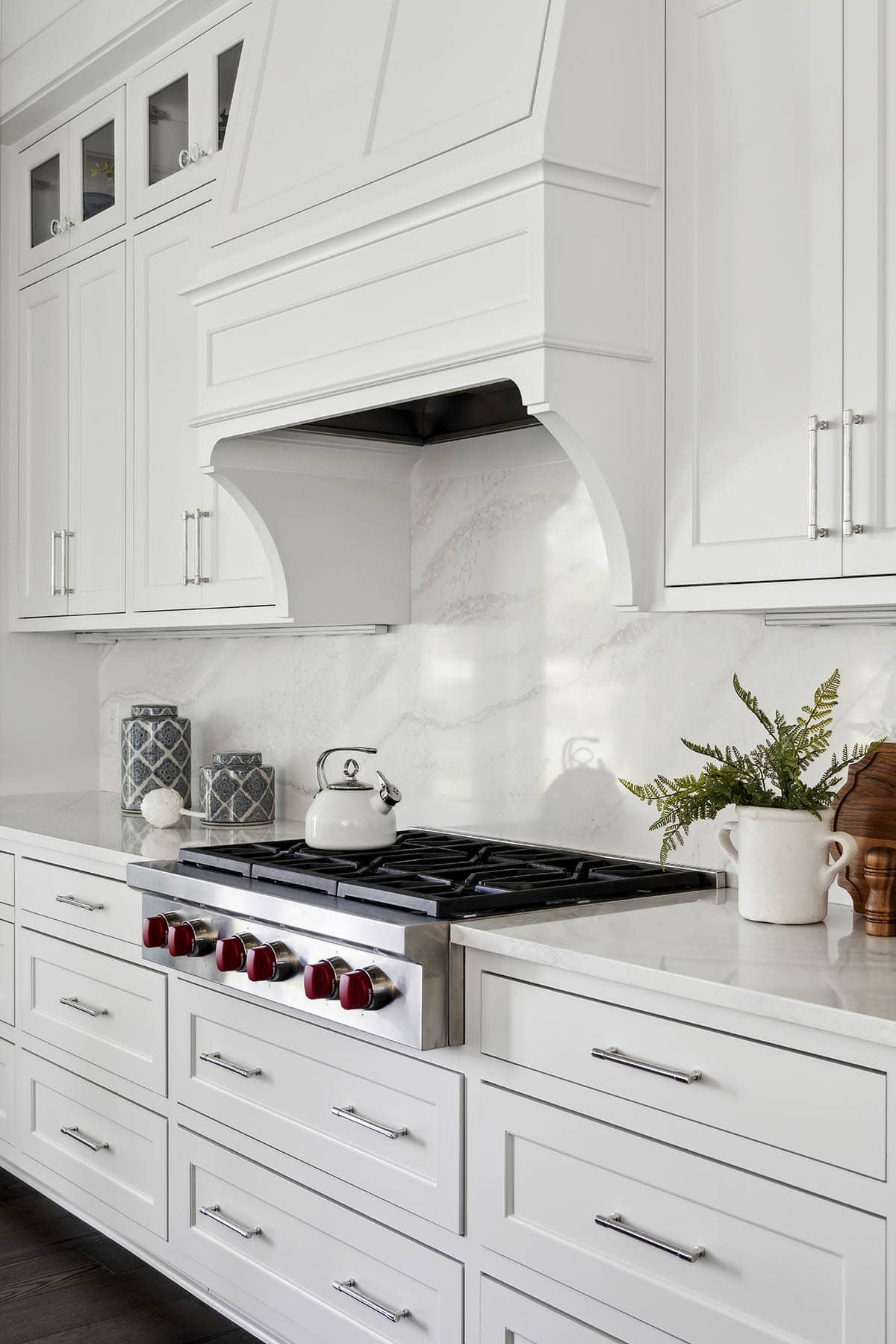 White curved range hood over gas cooktop with red knobs