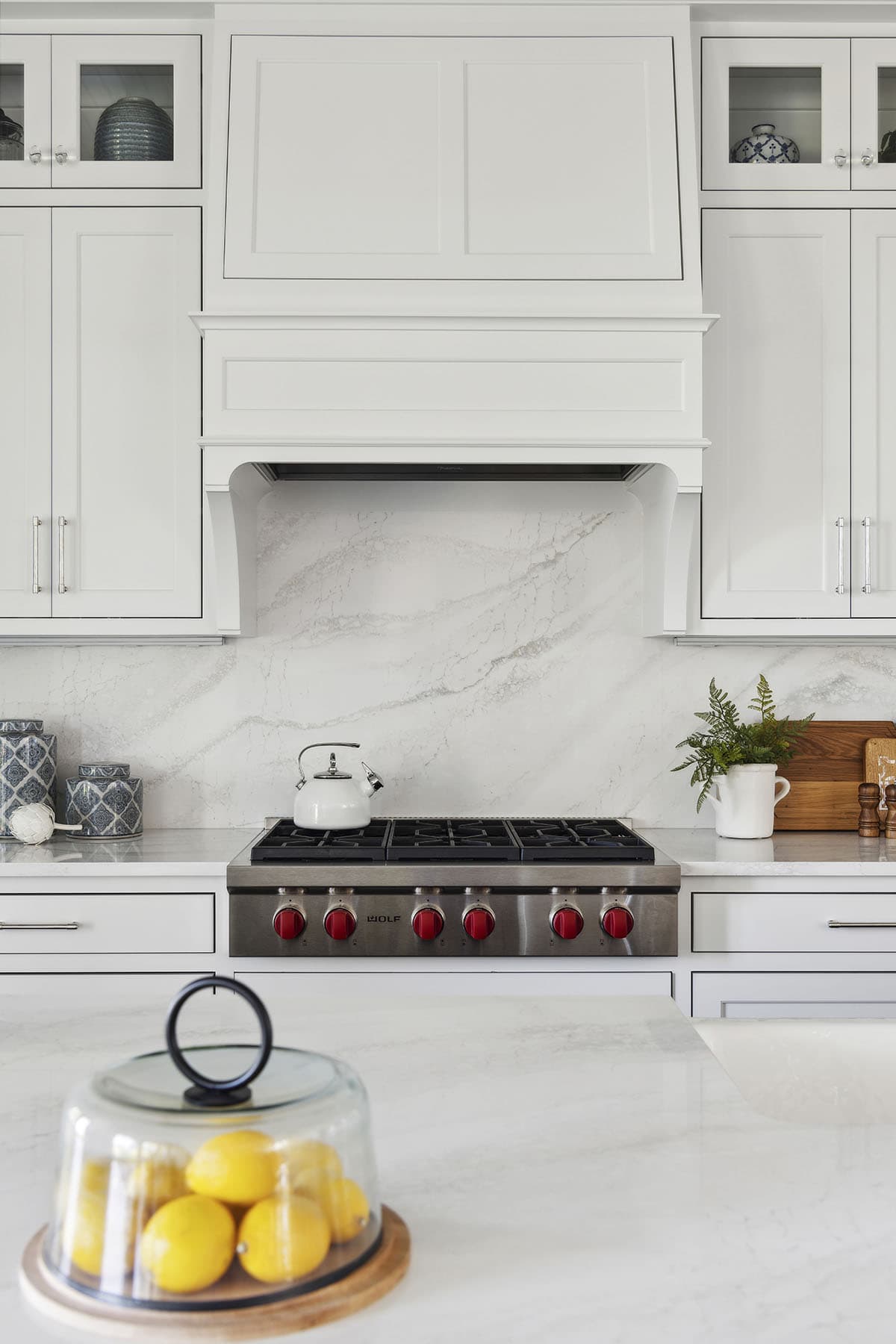 Marble backsplash behind red-knobbed range with hood detail