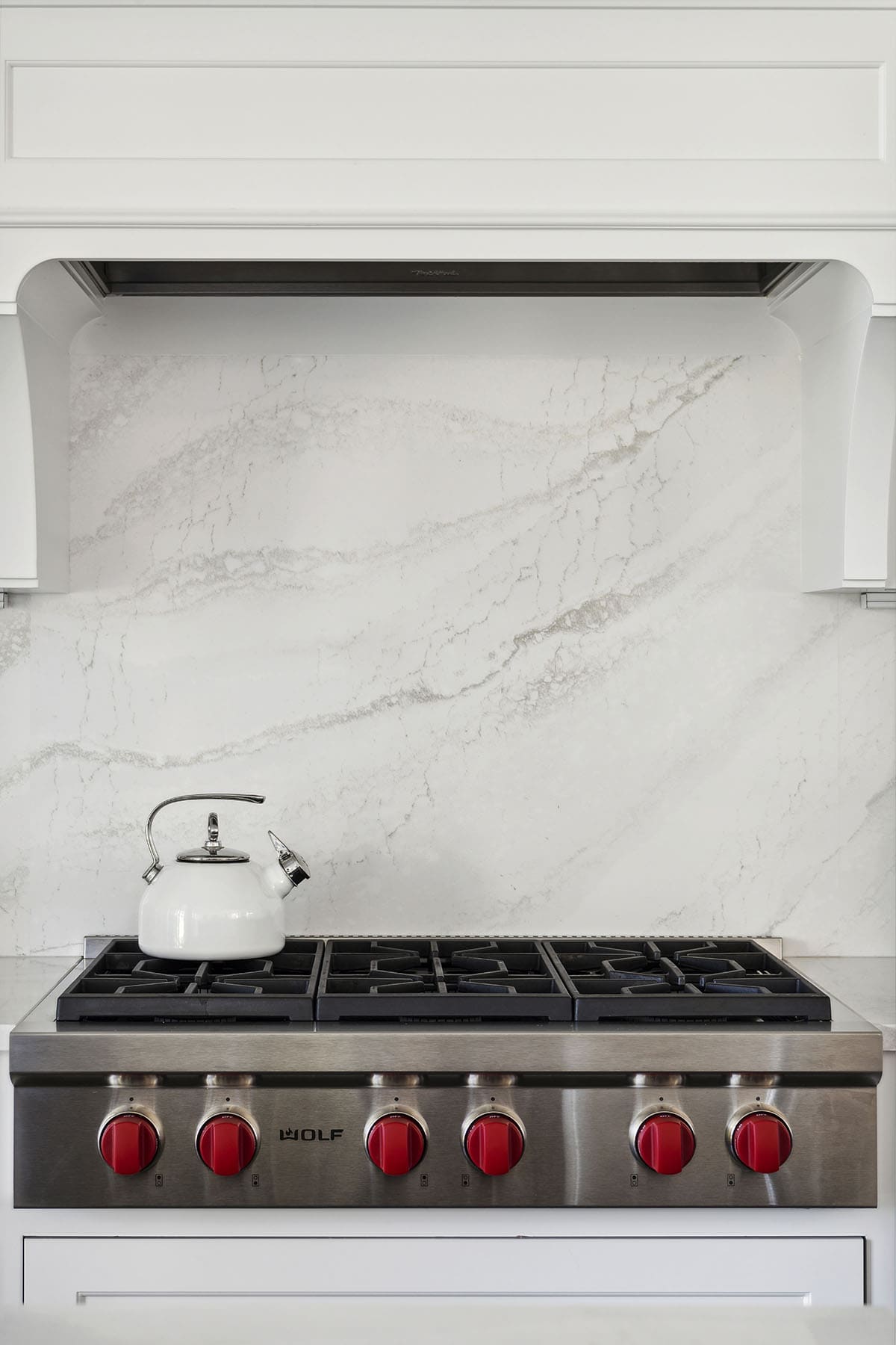 Close-up of Wolf gas range with red knobs and marble backsplash