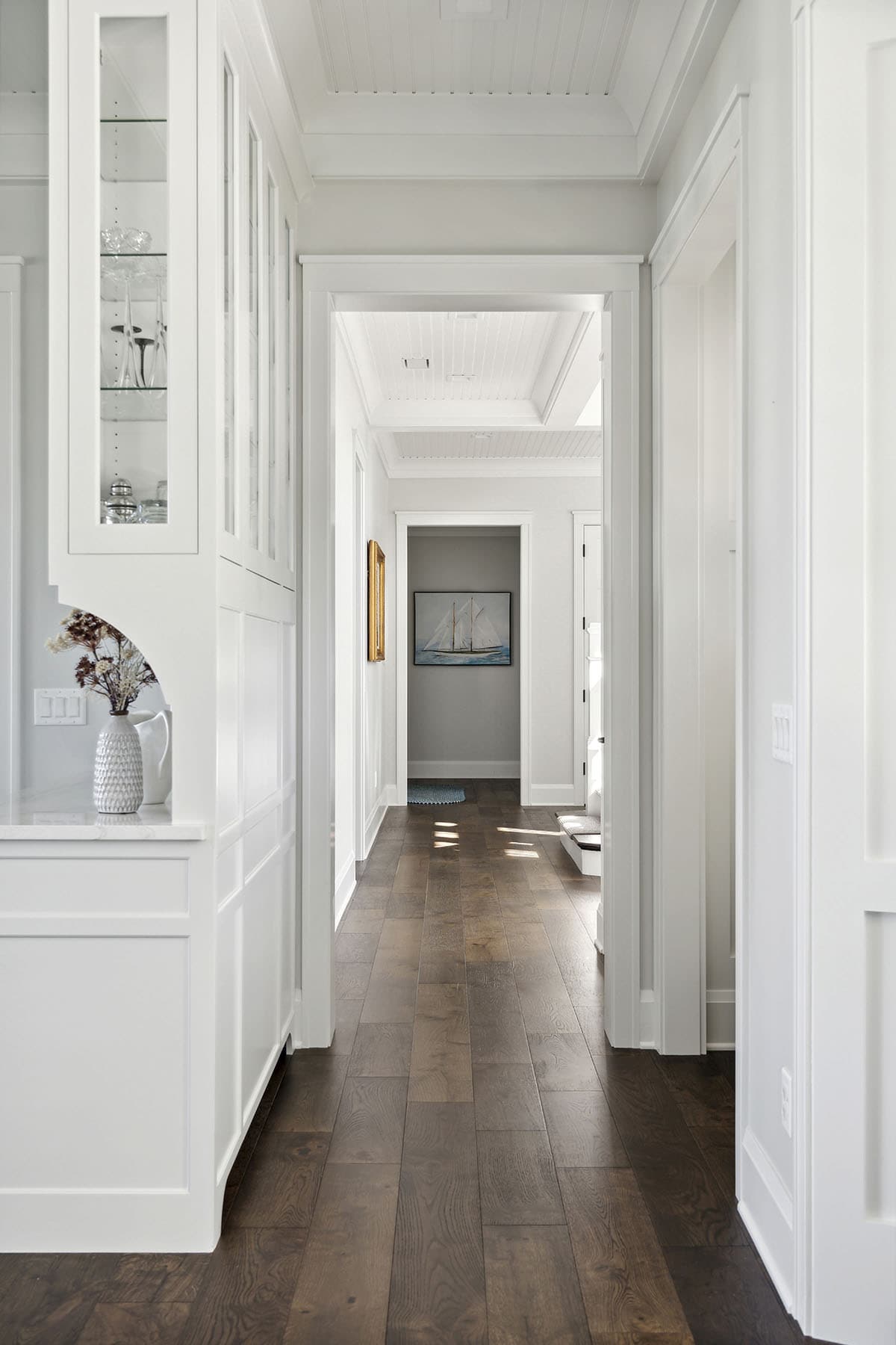 Hallway with dark wood floors leading to bedroom with sailboat art