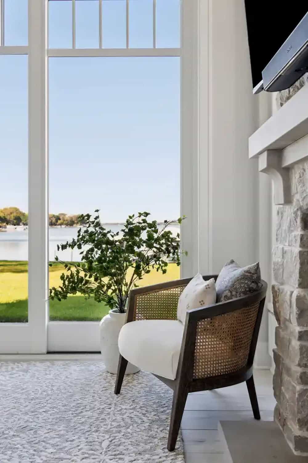 Cane armchair by window with lake view and fireplace