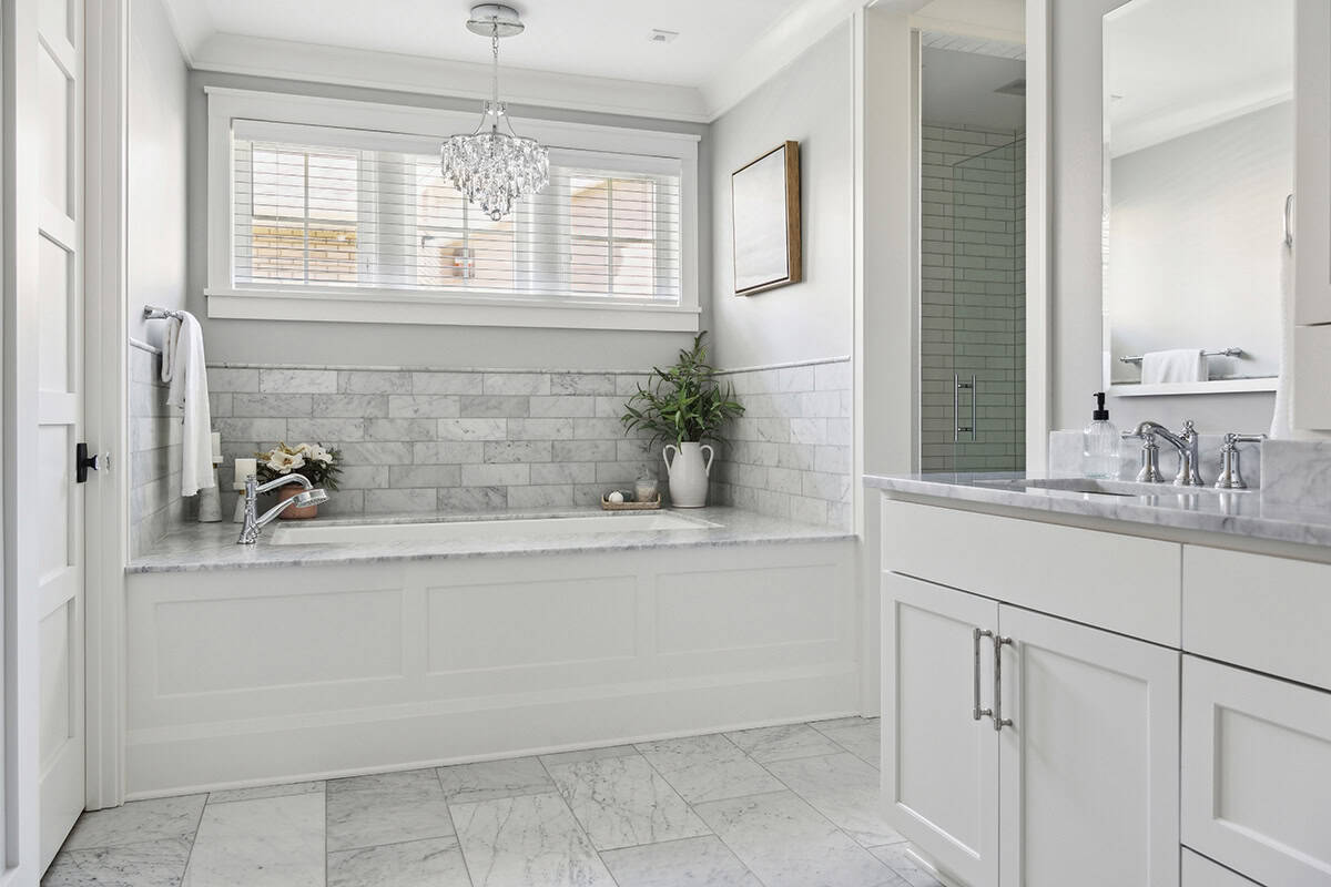 Marble-clad tub with chandelier and glass shower nearby