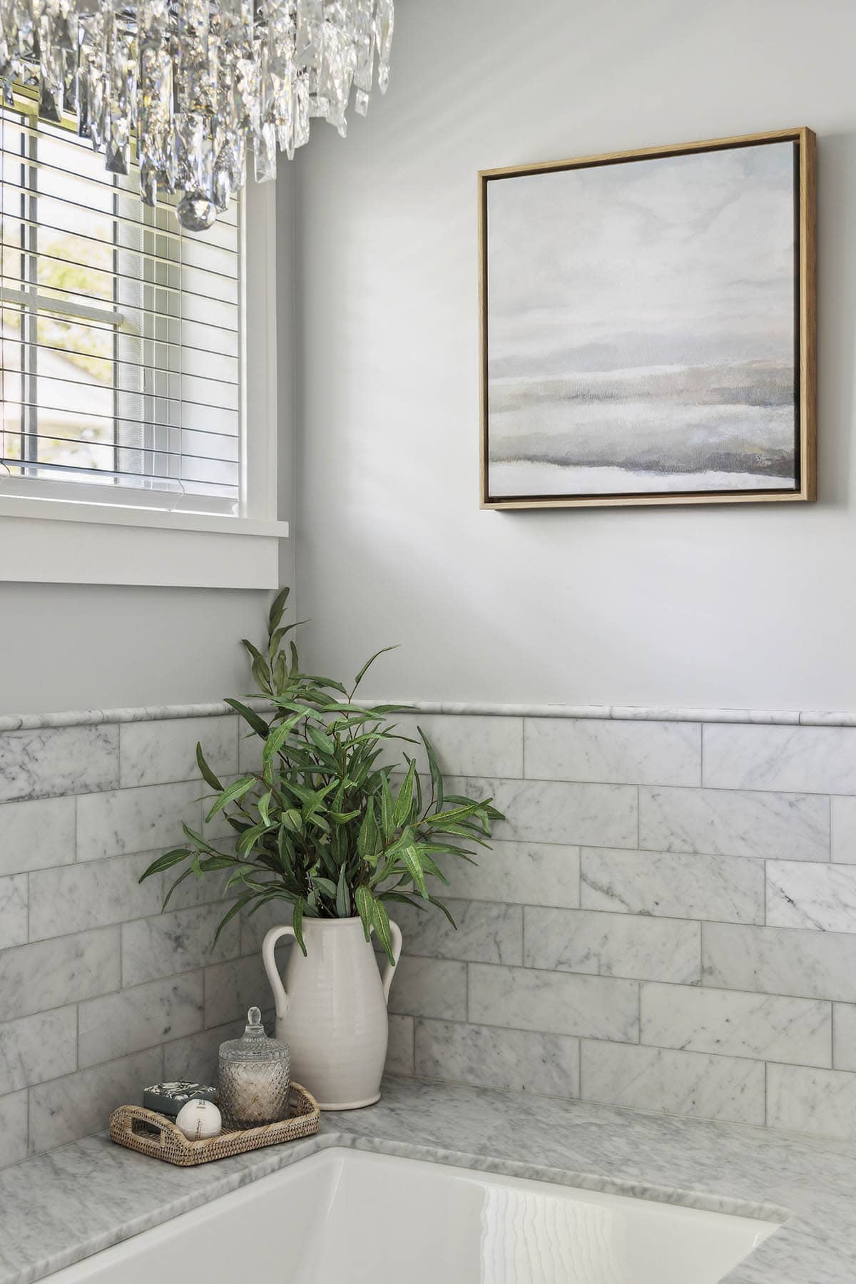 Corner of soaking tub with framed art and marble tile