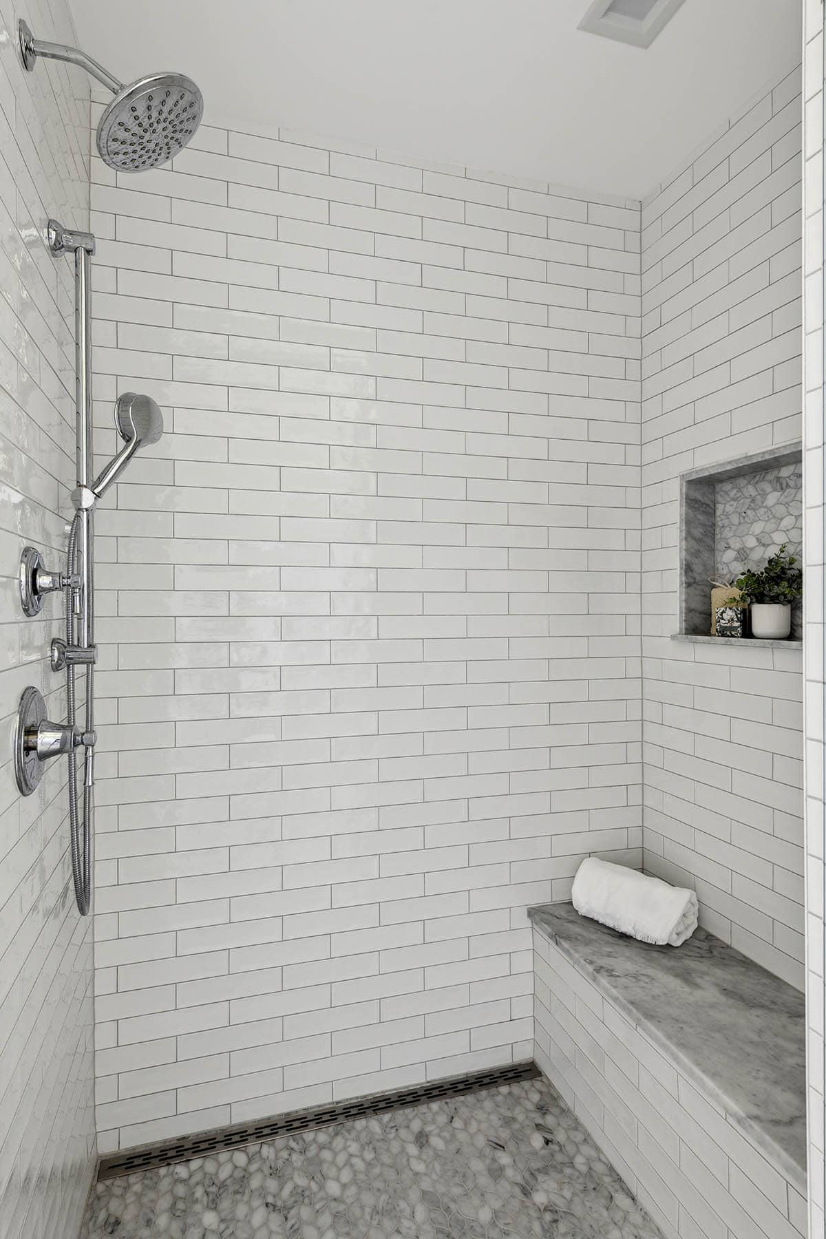 White subway tile shower with marble bench and niche