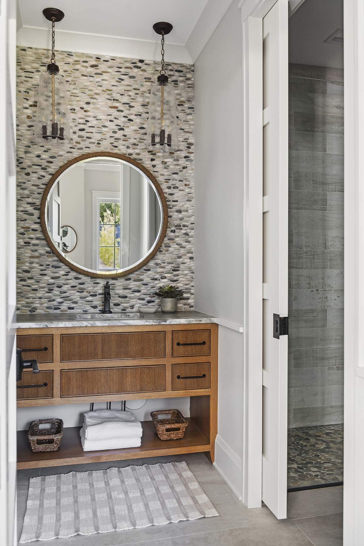 Powder room with pebble tile wall and round woven mirror