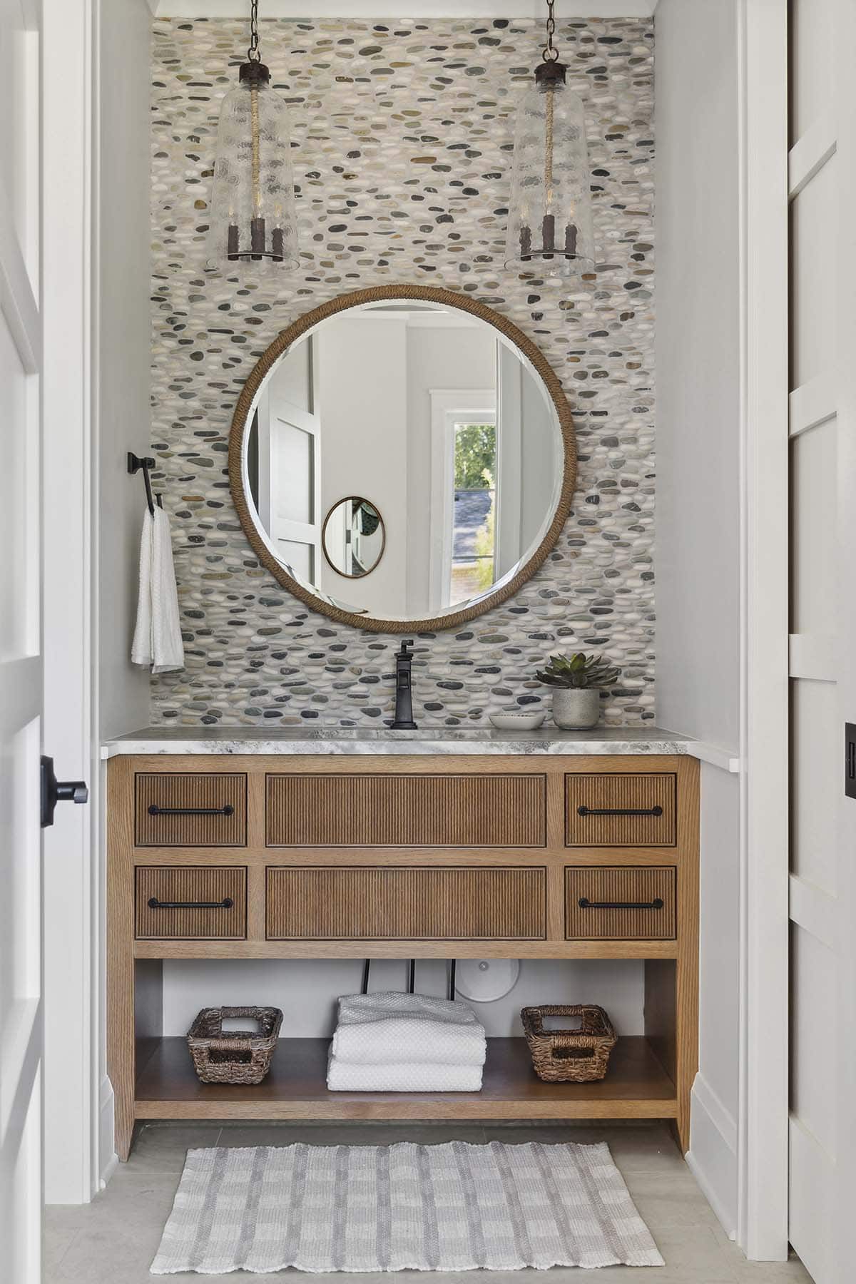 Pebble tile accent wall with wood vanity and pendant lights