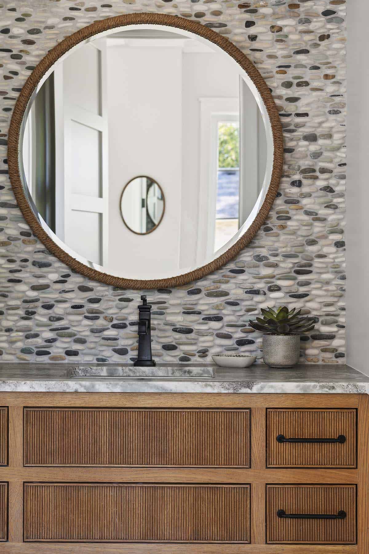 Close-up of round mirror and pebble tile in powder room