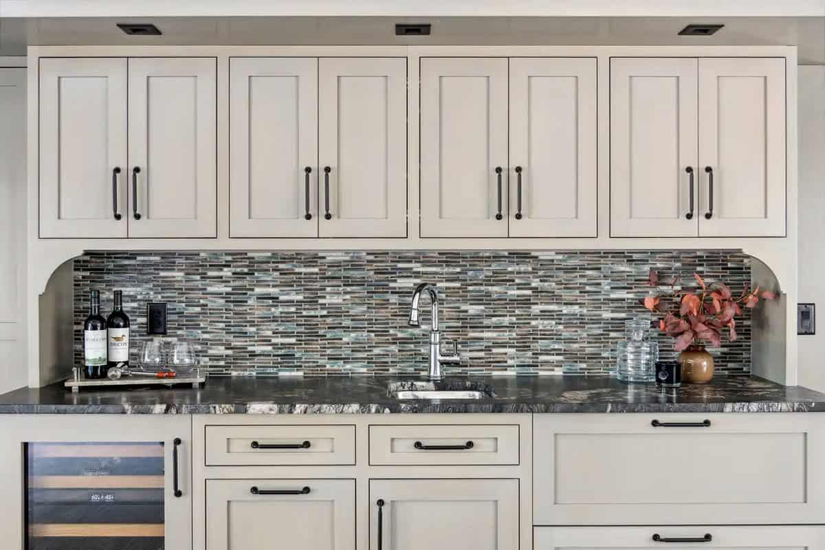Wet bar counter with wine bottles and glass mosaic backsplash
