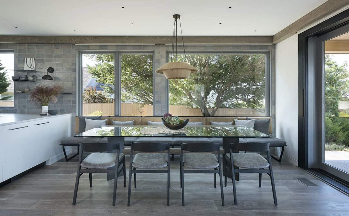 Dining nook with glass table, black chairs, and built-in banquette seating beneath large windows and a woven pendant light