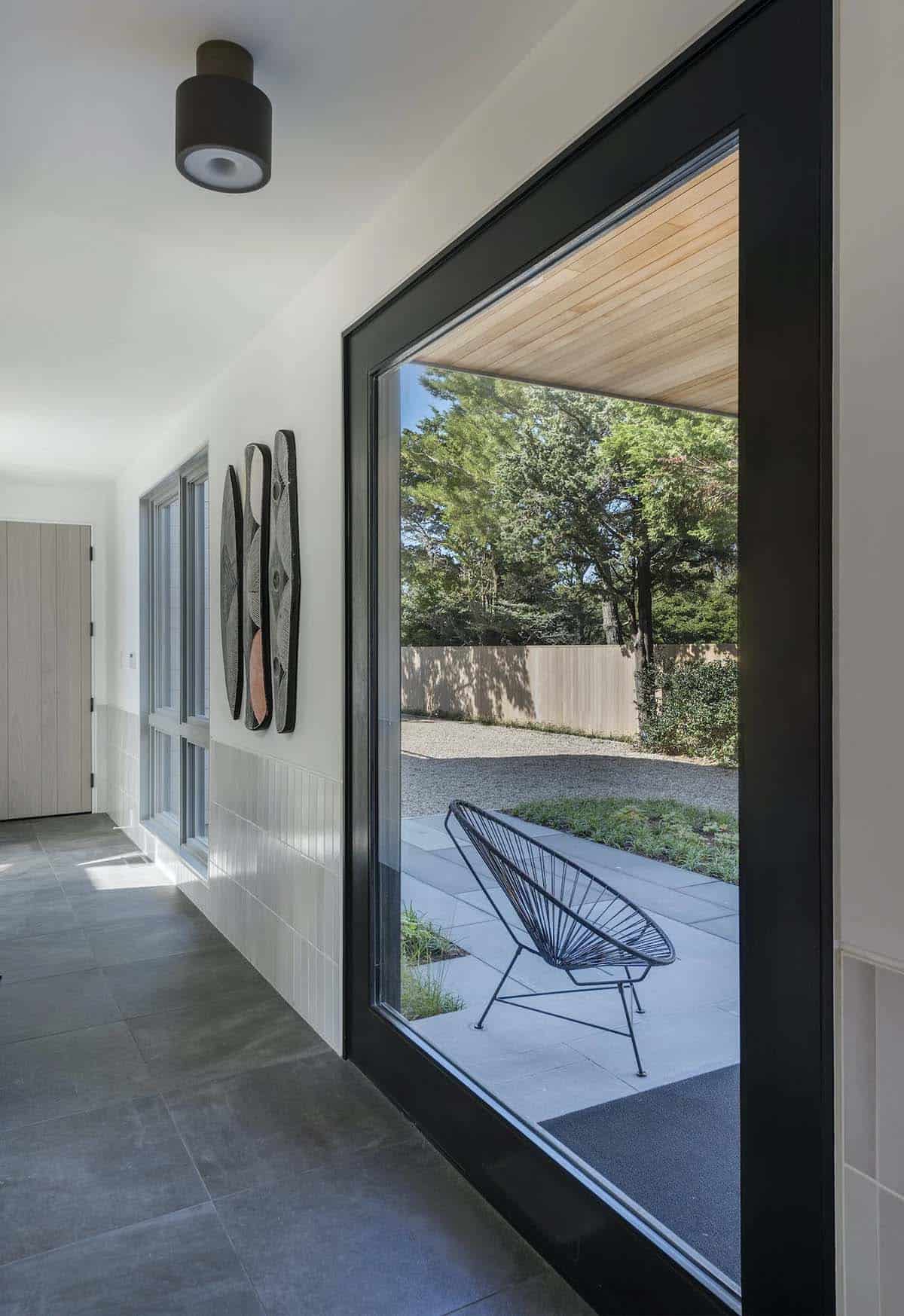 Hallway with framed wall art leading to a large angled window showing a black wire chair on a stone patio