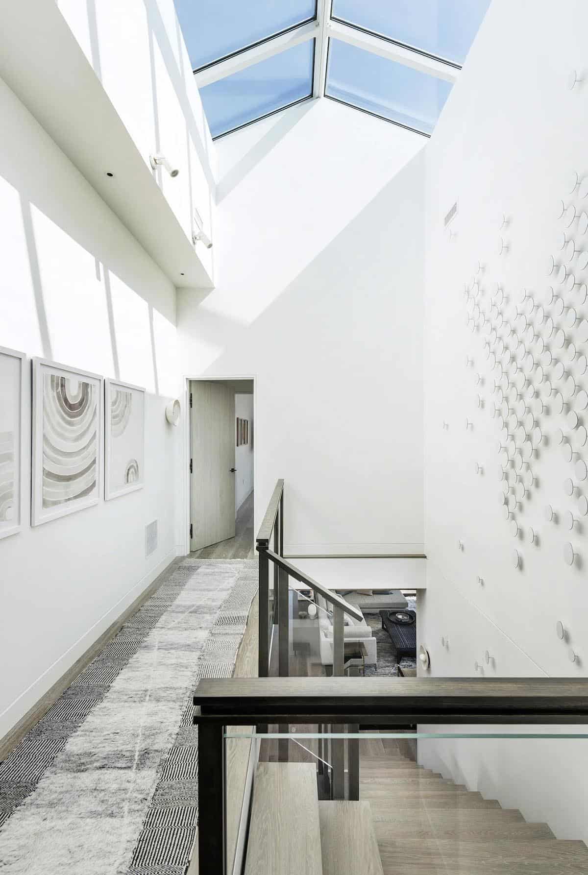 Double-height stairwell with a pyramid skylight, gallery wall, textured runner rug, and dotted wall art installation