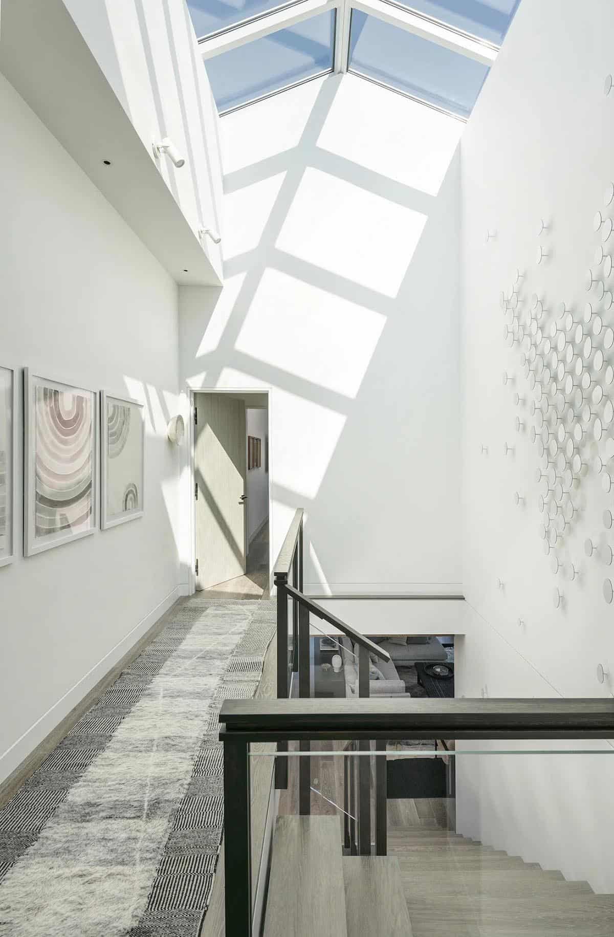 Sunlit stairwell with pyramid skylight casting geometric shadows, framed art, and a dotted wall sculpture