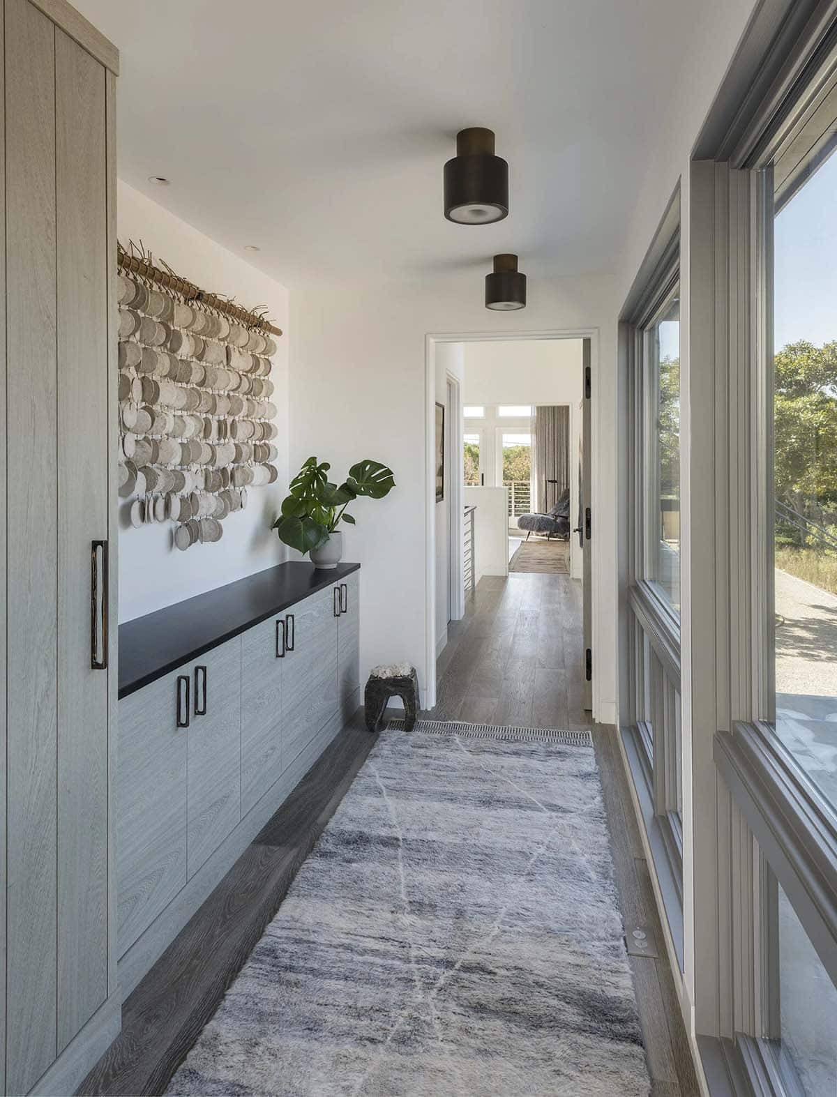 Long hallway with woven wall hanging, black cabinetry, gray runner rug, and floor-to-ceiling windows