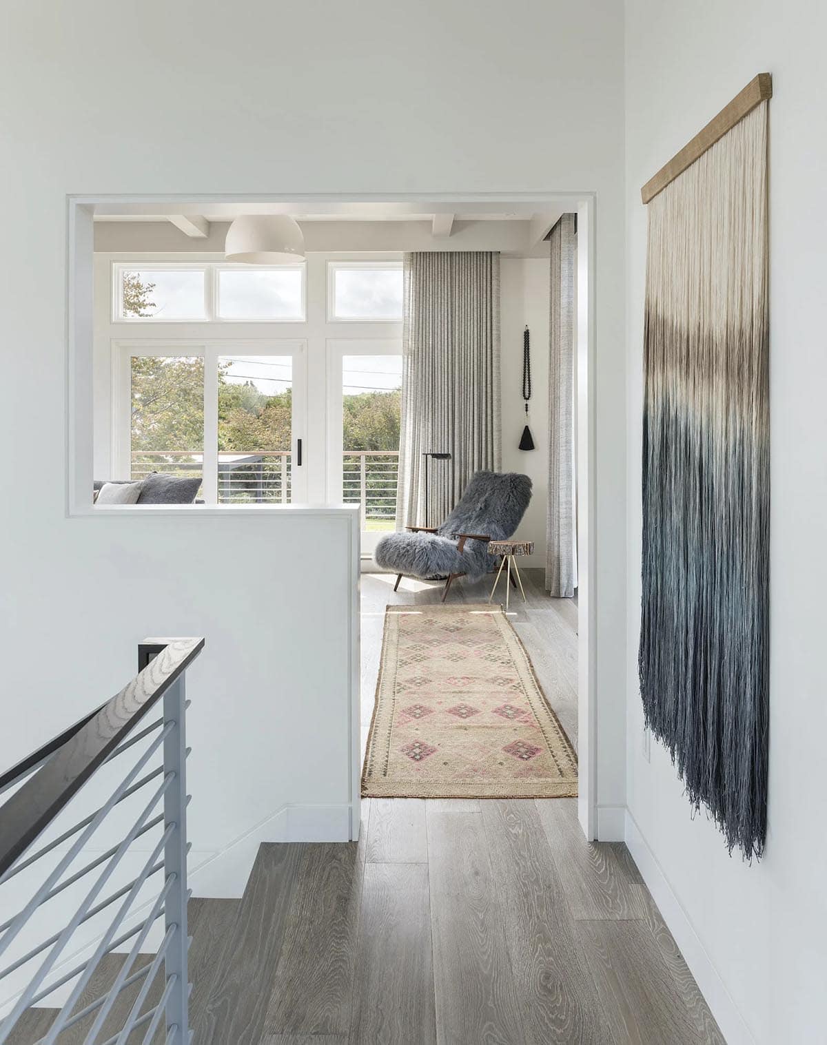 View from hallway into a sitting room with a fuzzy gray chair, striped rug, and a fringed ombre wall hanging