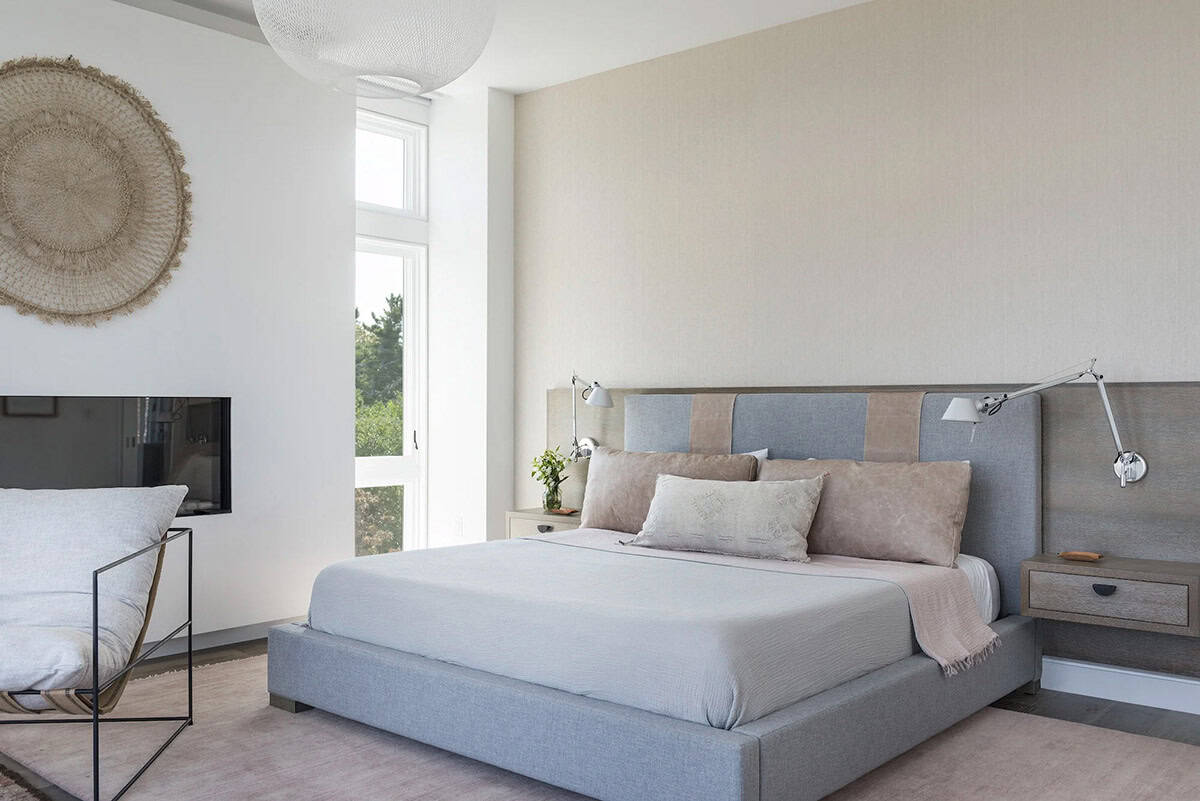 Bedroom with gray upholstered bed, floating wood nightstands, woven wall disc, and a wall-mounted fireplace
