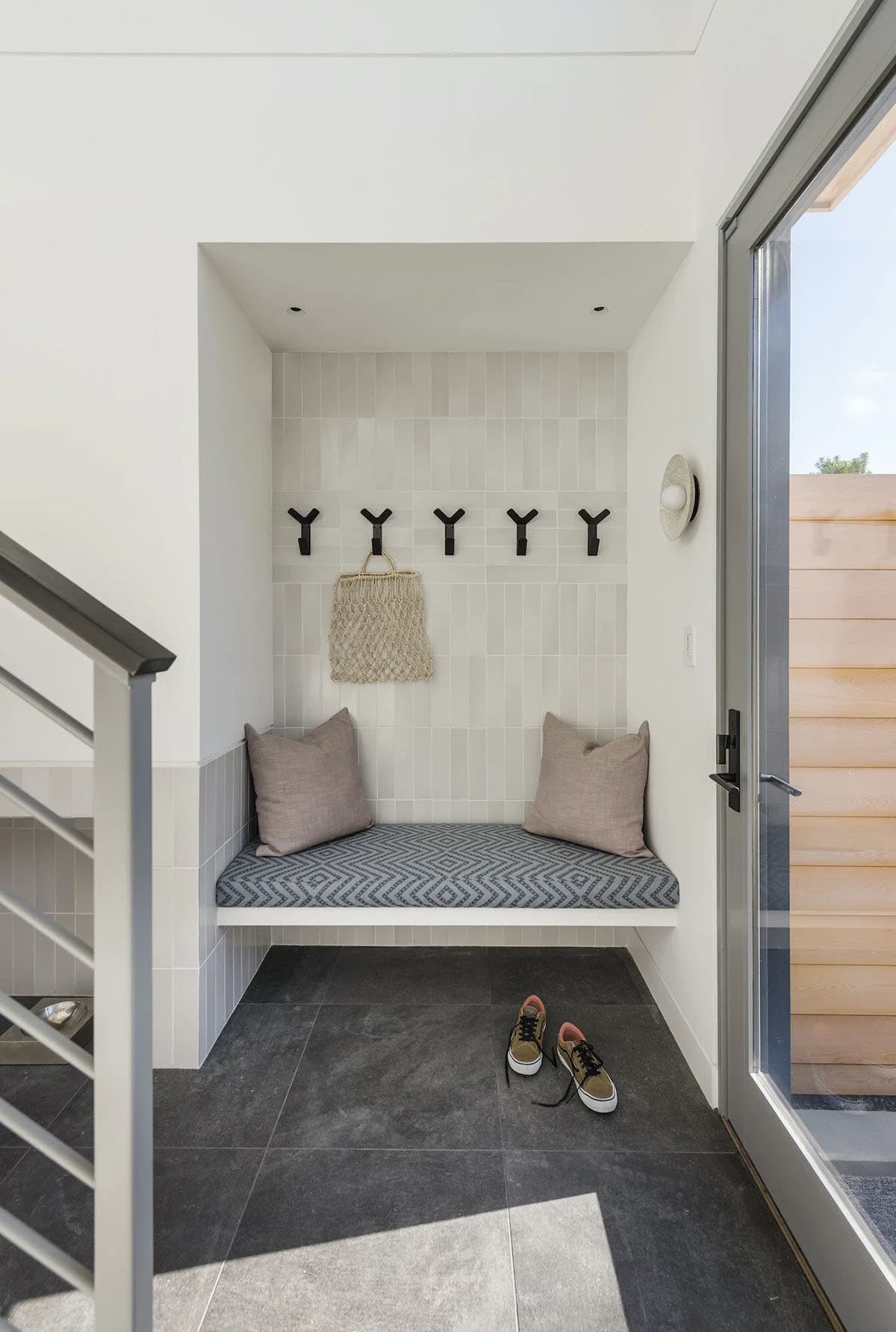 Built-in mudroom bench nook with patterned cushion, black hooks, and tile backsplash beside a glass entry door