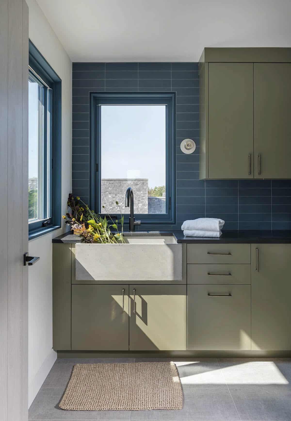 Laundry room with olive-green cabinetry, concrete farmhouse sink, and blue subway-tiled accent wall with window