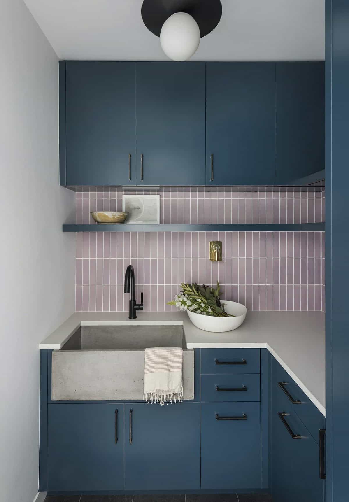 Small utility sink nook with navy cabinetry, concrete sink, and pink vertical tile backsplash